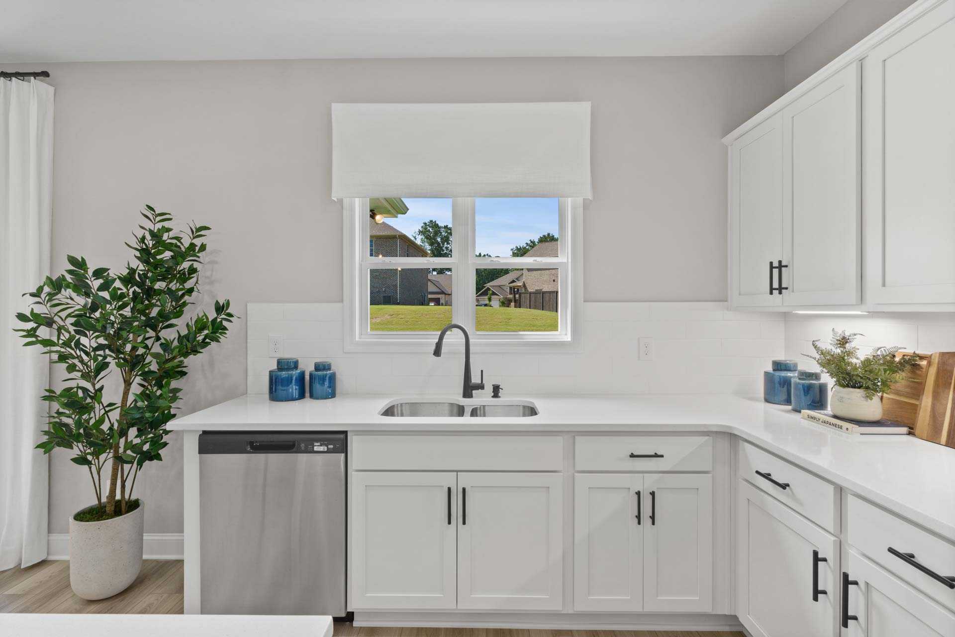 Spacious white kitchen at Creek Grove in New Market Alabama with shaker cabinets, quartz counters, stainless sink and backyard view