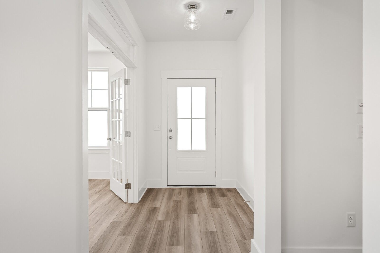 Bright entry foyer with white glass-paneled door, open rooms, and hardwood floors in Davidson Homes The Ash C, Mt. Juliet, Tennessee