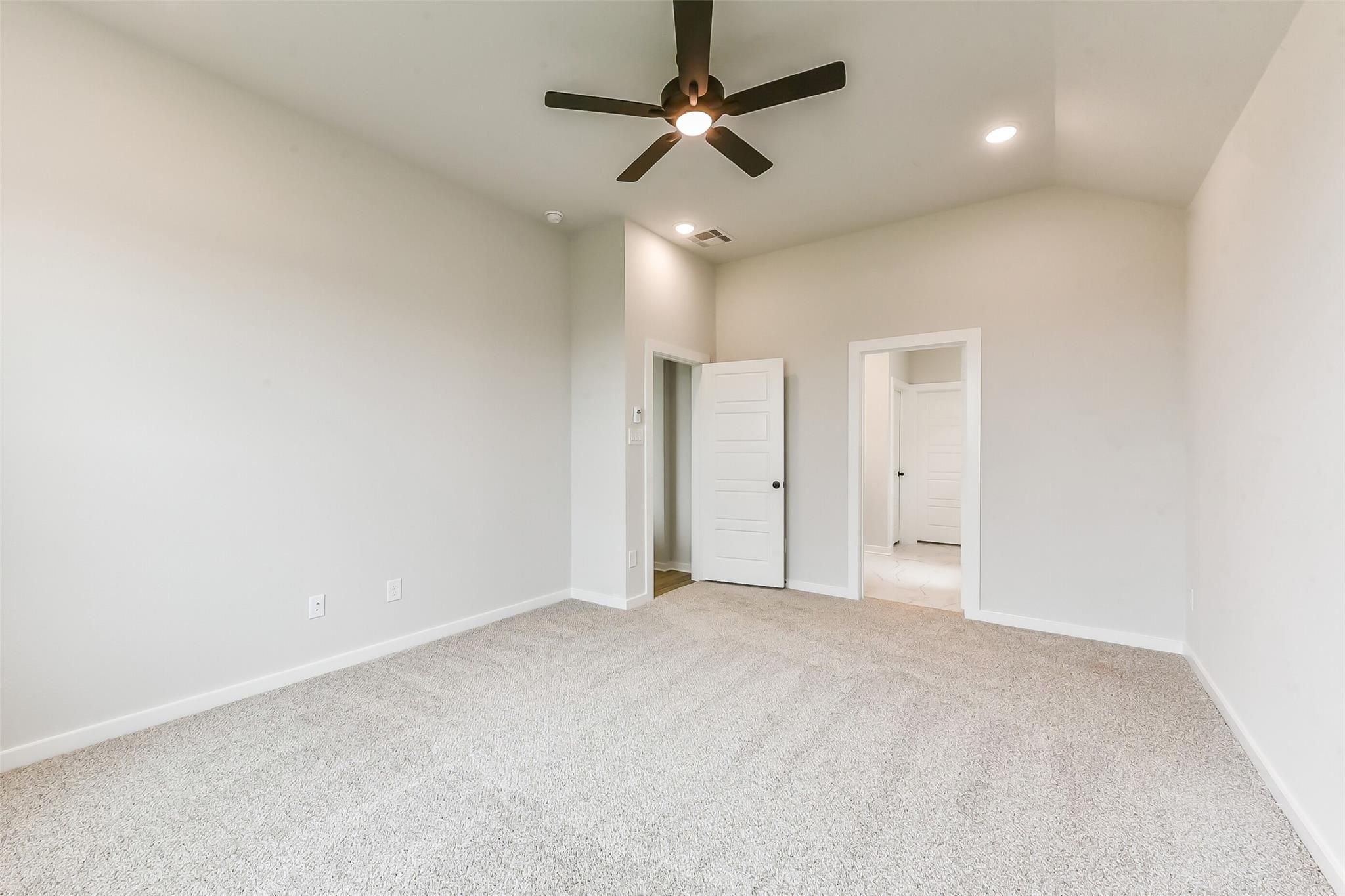 Spacious bedroom featuring ceiling fan, en-suite bathroom access, and neutral carpet in Davidson Homes Sequoia C, Crosby, Texas