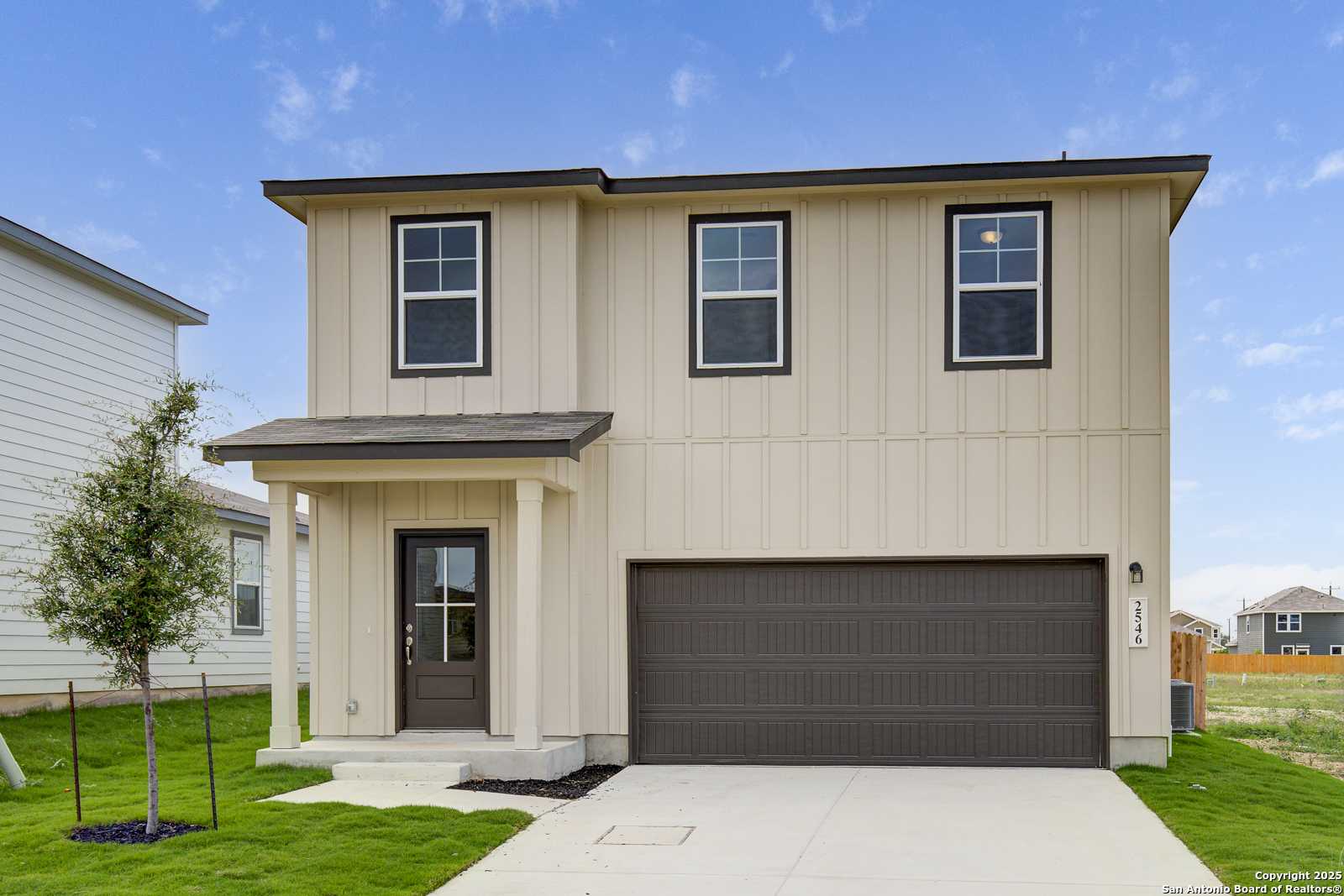 Modern two-story beige home with dark roof, 2-car garage, and covered porch in Applewhite Meadows, San Antonio