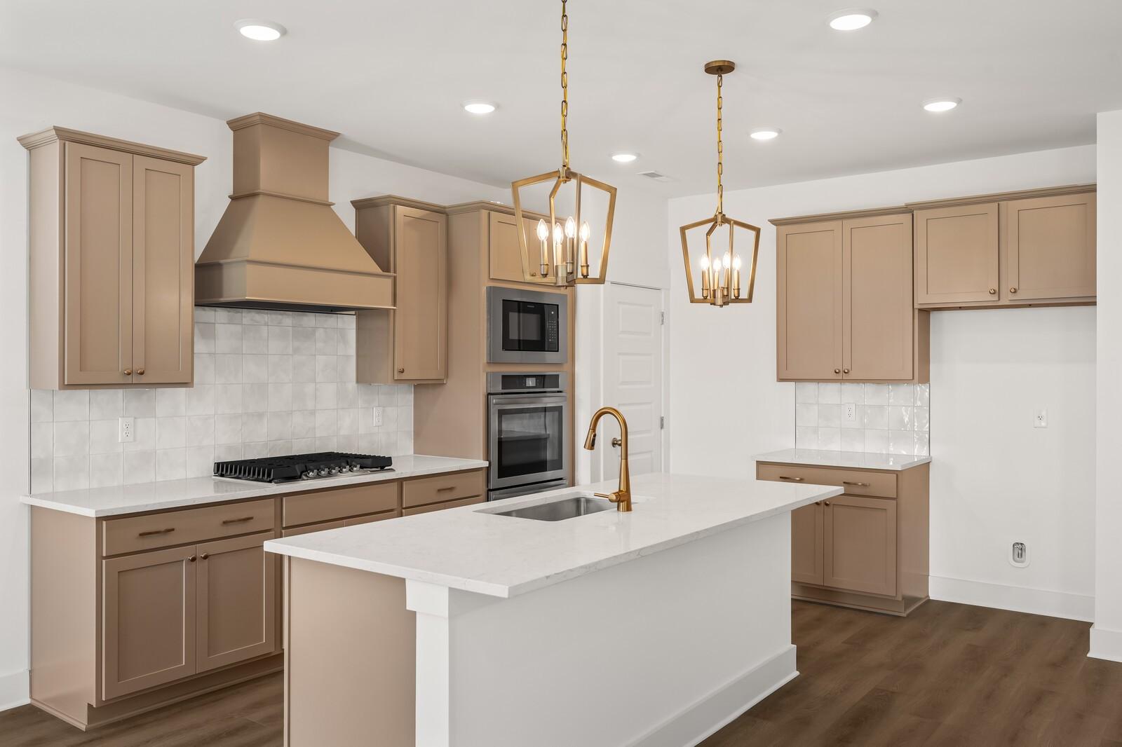 Modern kitchen with beige shaker cabinets, white quartz island, gas stovetop, double ovens, and gold pendant lights in The Ash A floor plan