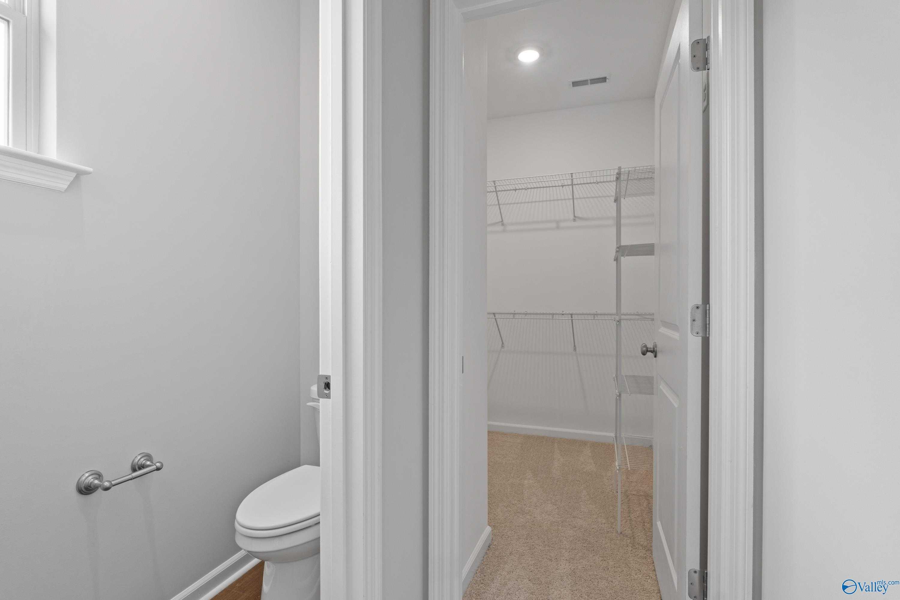 Bright white powder room with toilet and open closet shelving in The Dorado floor plan, Davidson Homes, Athens Alabama