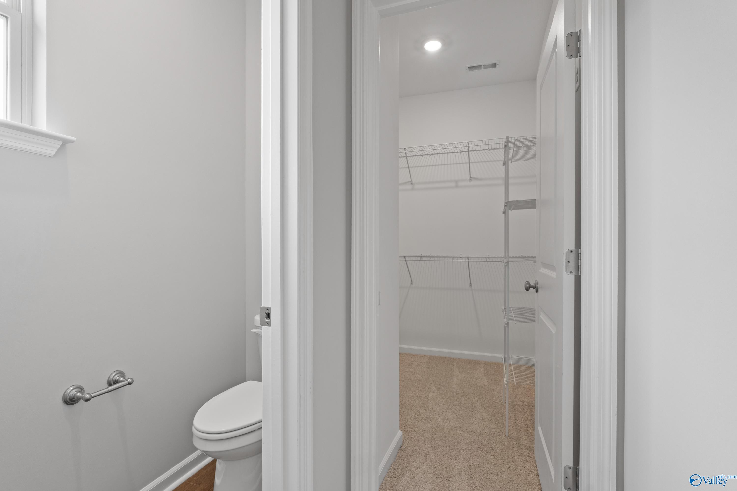 Modern bathroom with white toilet and adjacent walk-in closet featuring wire shelving in Davidson Homes The Dorado, Athens Alabama