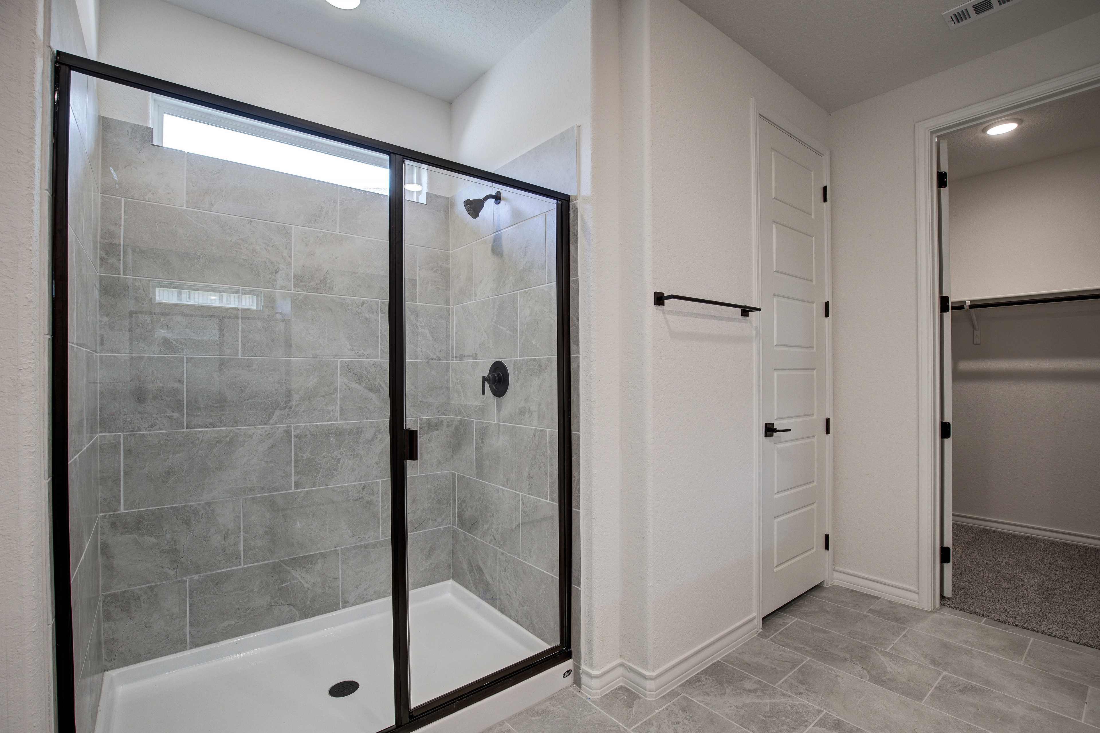 Modern master bathroom in The Lanier with frameless glass shower, gray tile walls, and walk-in closet access