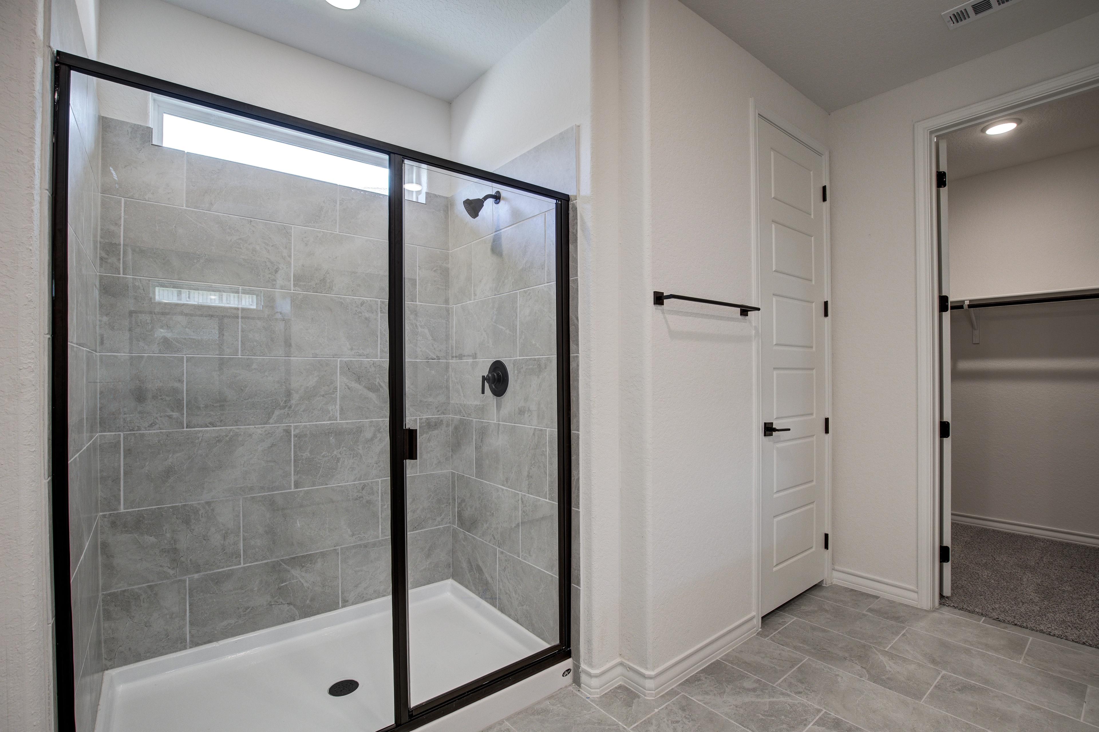 Spacious master bathroom in The Lanier with frameless glass walk-in shower, gray tile walls, and adjacent walk-in closet