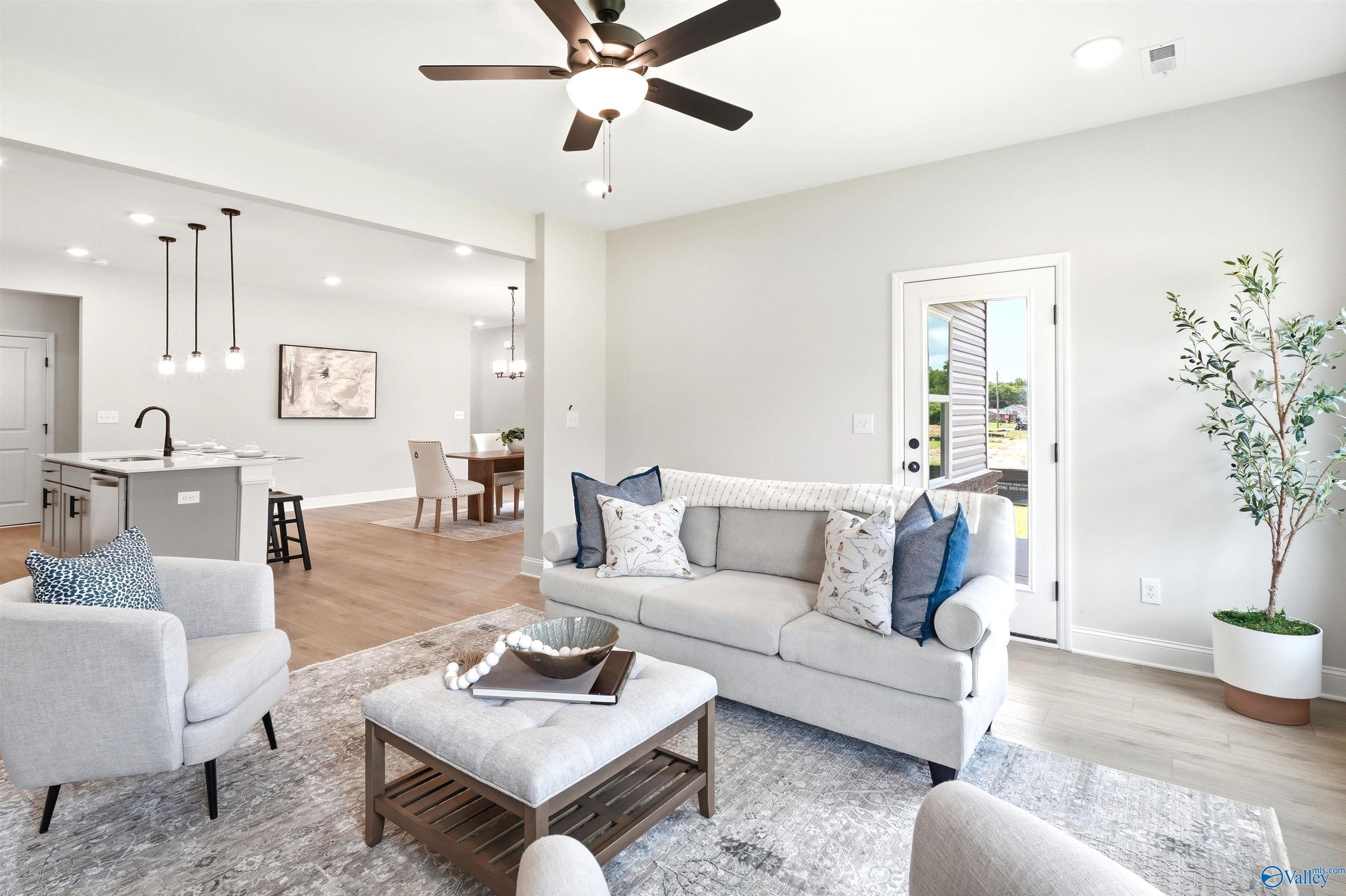 Bright open-concept living room with sofa and ceiling fan overlooking kitchen island in The Russell A plan at Spragins Cove, Huntsville
