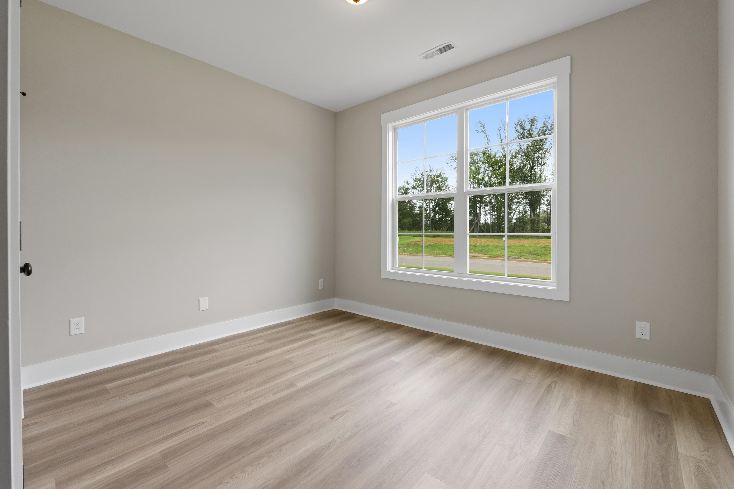 Spacious empty bedroom in The Oxford B: beige walls, large white-framed window with lawn view, light oak hardwood floors