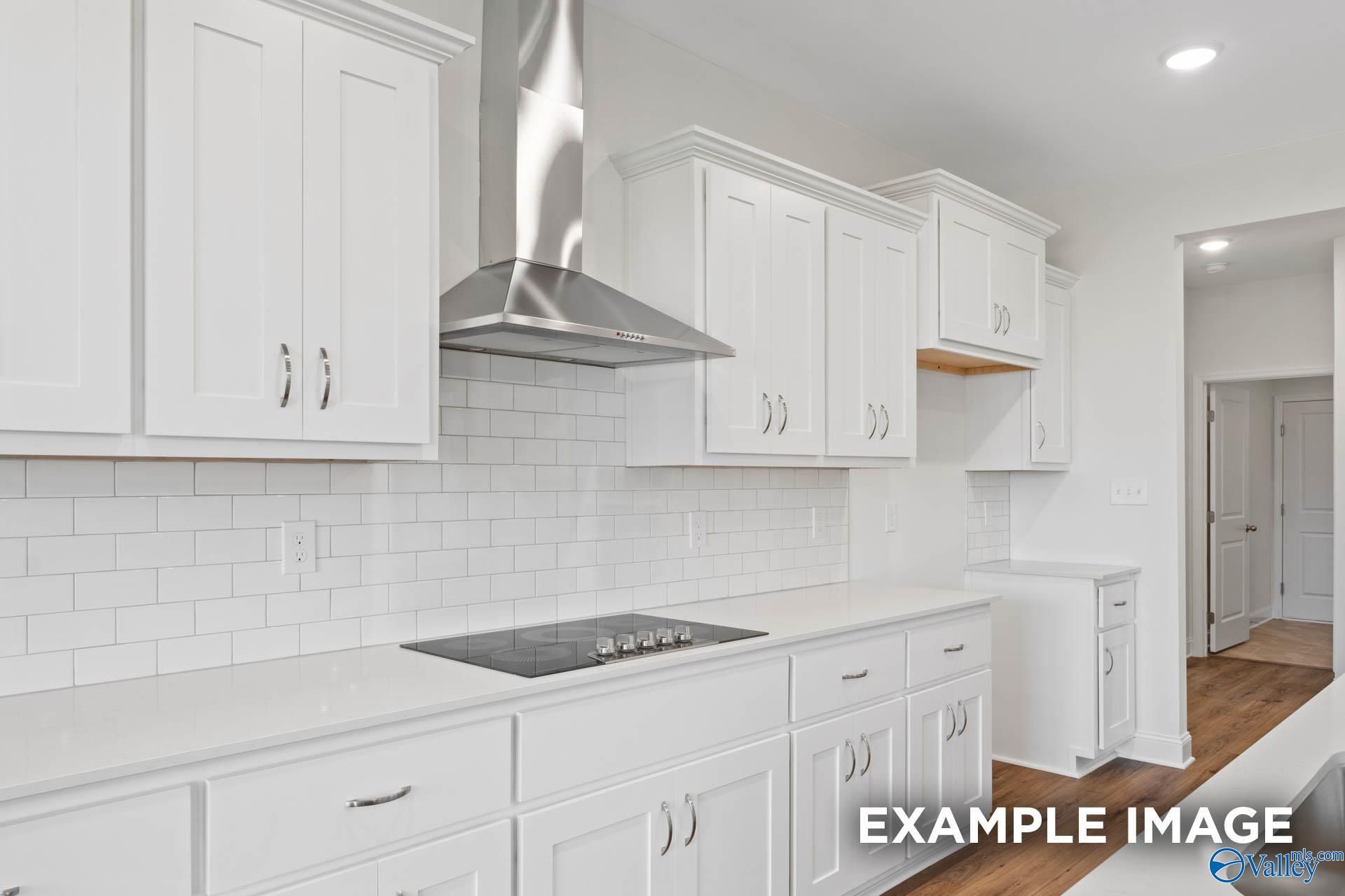 Modern white kitchen with subway tile backsplash, stainless hood, and induction cooktop in Davidson Homes The Oxford, Huntsville AL