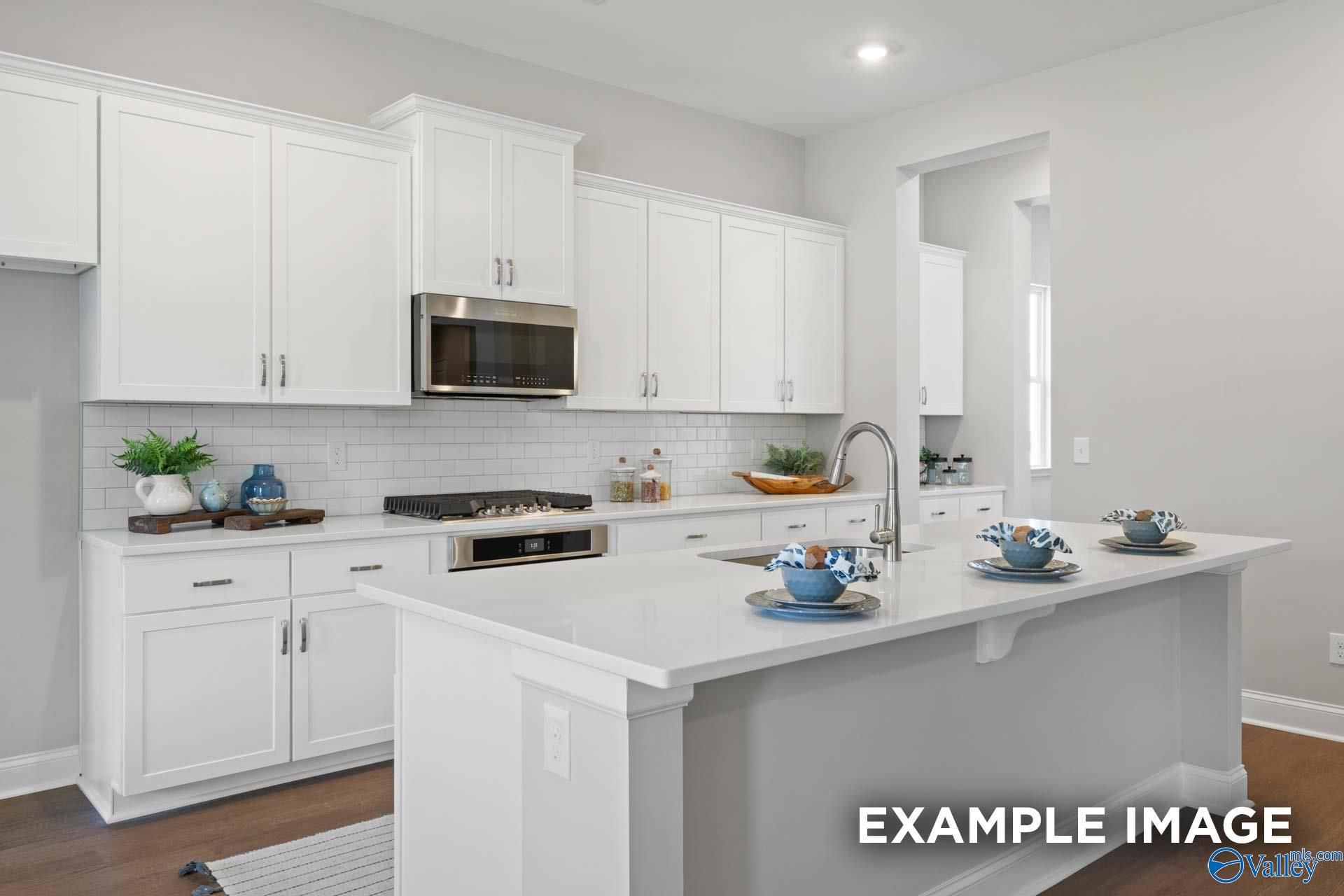 Modern white shaker kitchen featuring subway tile backsplash, quartz island, stainless appliances in The Haven E, Owens Cross Roads, AL