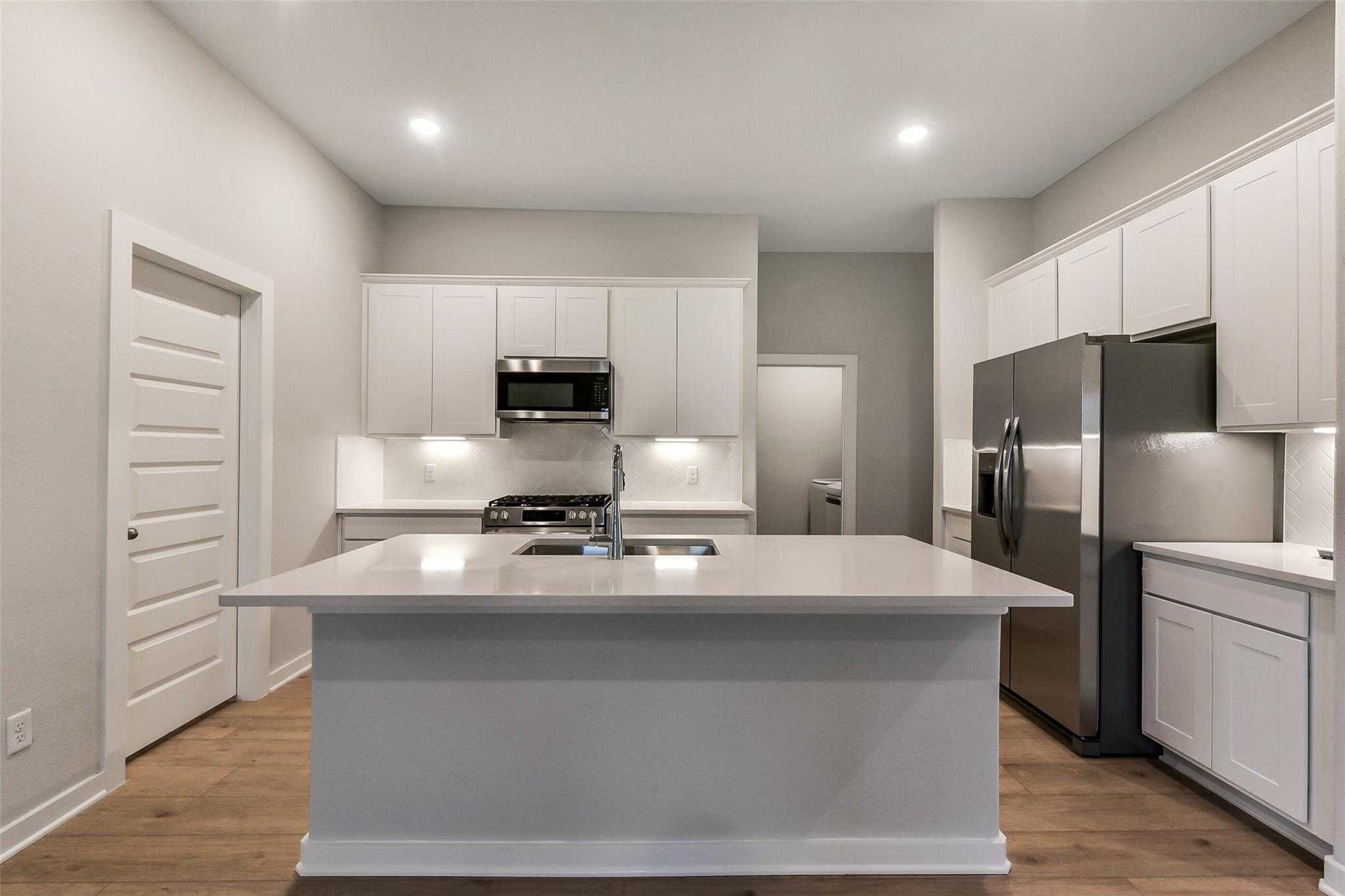 Modern white kitchen with quartz island sink, stainless steel appliances, and open layout in Davidson Homes The Laguna B, Sunterra, Katy, Texas