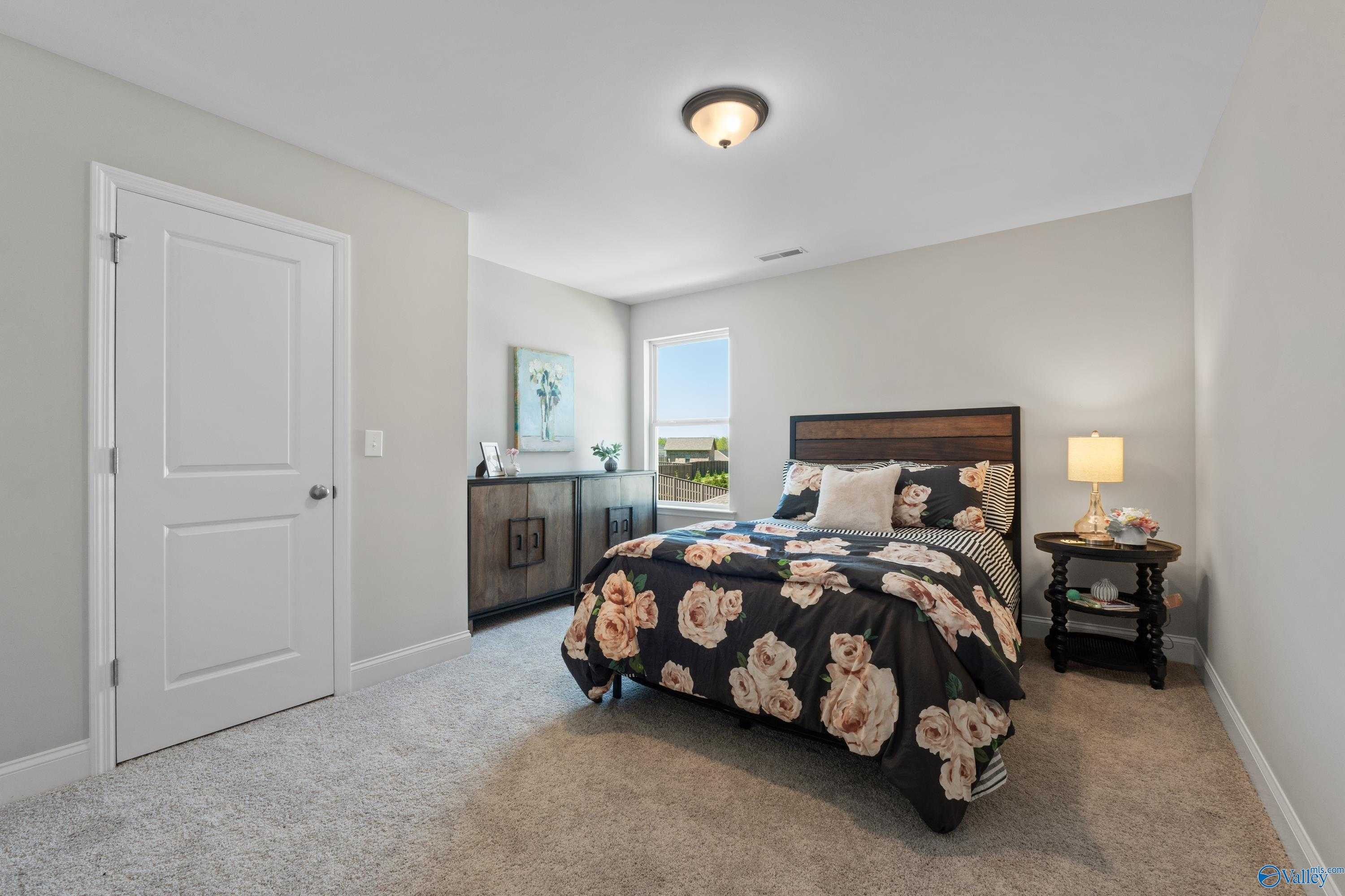 Cozy bedroom with floral rose bedding on wooden headboard bed, nightstands, lamps, and window view in Evermore Homes The Haven, Owens Cross Roads