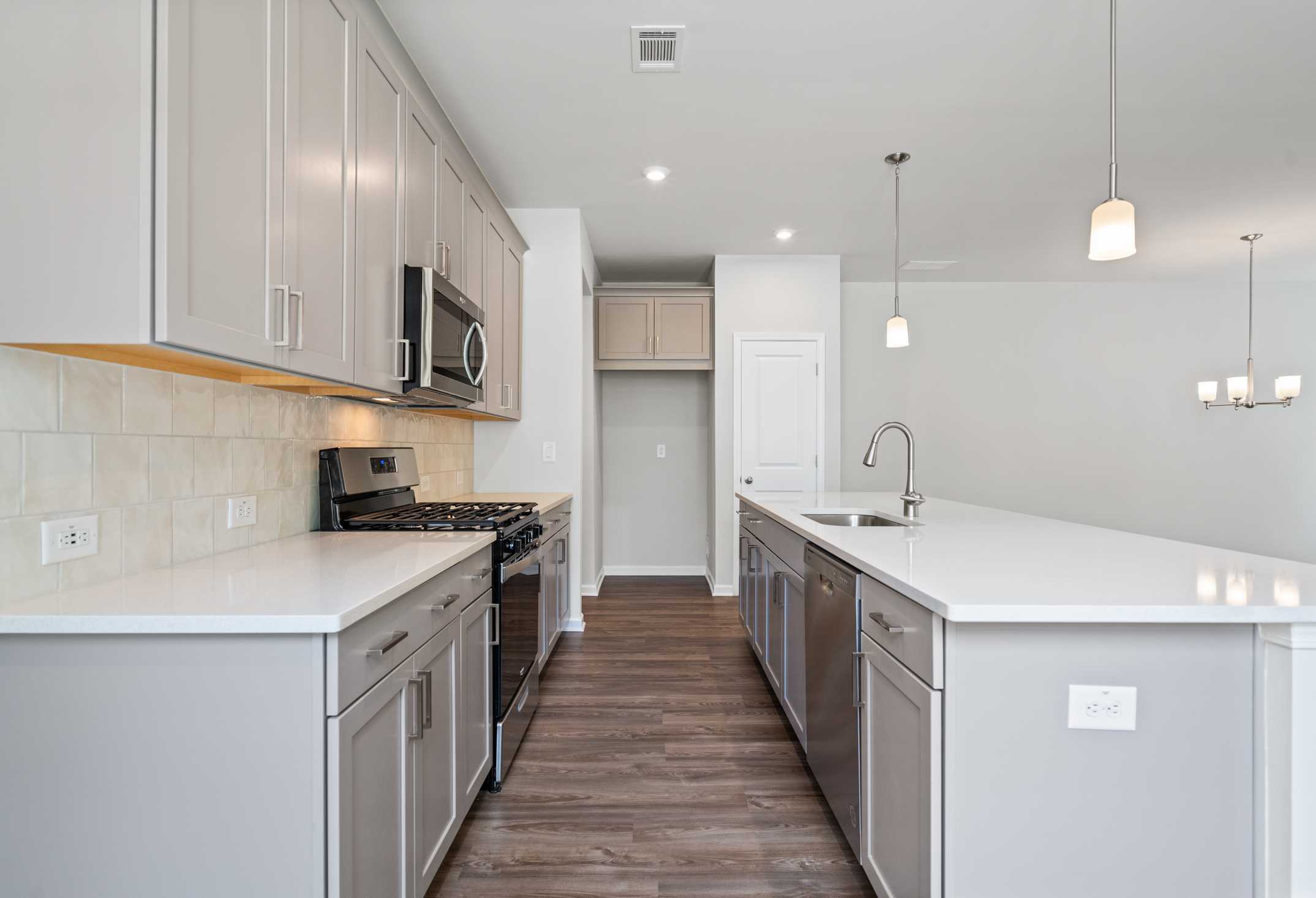 Spacious kitchen in The Cary A home featuring light gray cabinets, white quartz island, stainless steel appliances, and wood flooring