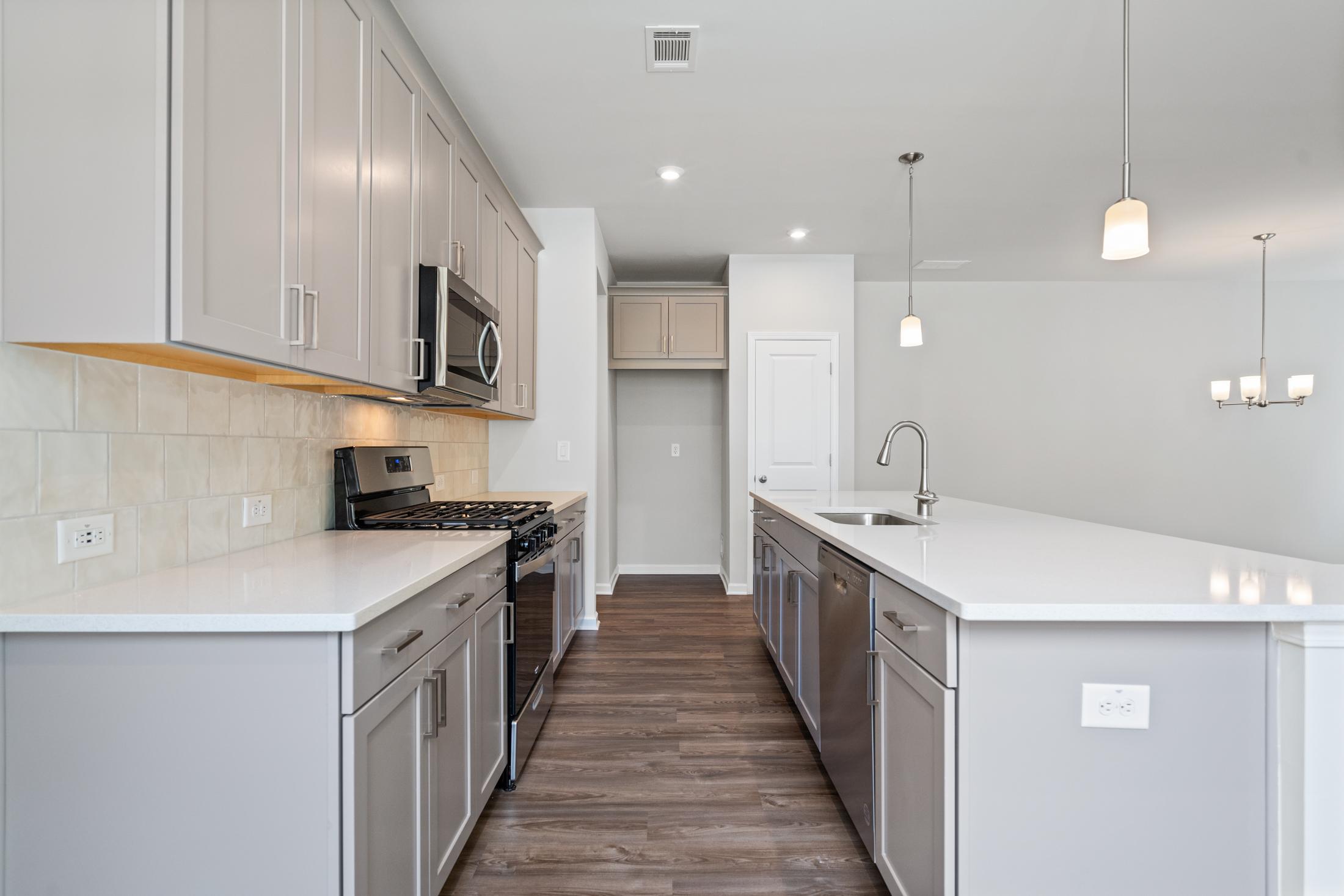 Spacious kitchen in The Cary A home featuring light gray cabinets, white quartz island, stainless steel appliances, and wood flooring