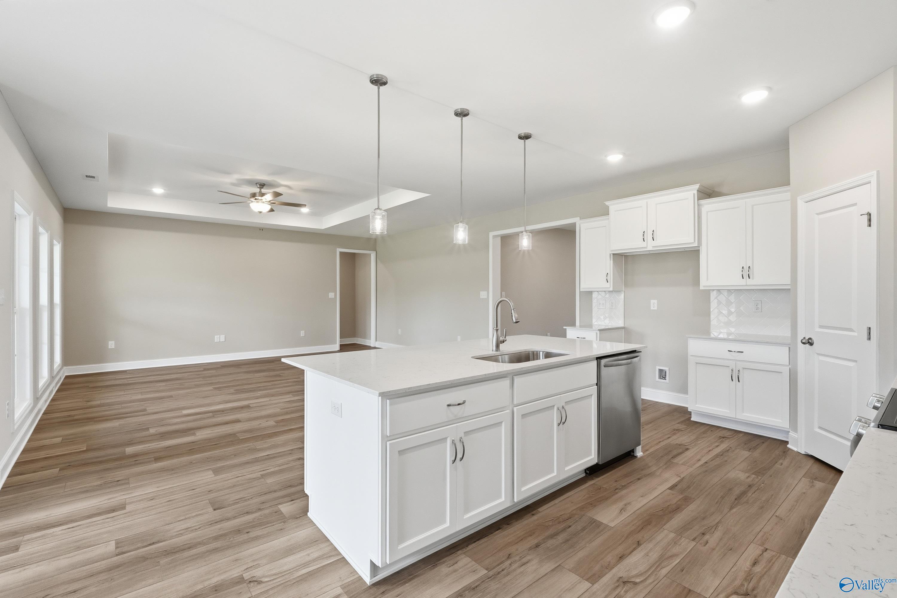 Modern open-concept kitchen with white island, stainless dishwasher, wood floors, and pendant lights in Davidson Homes The Harrison B, Decatur AL