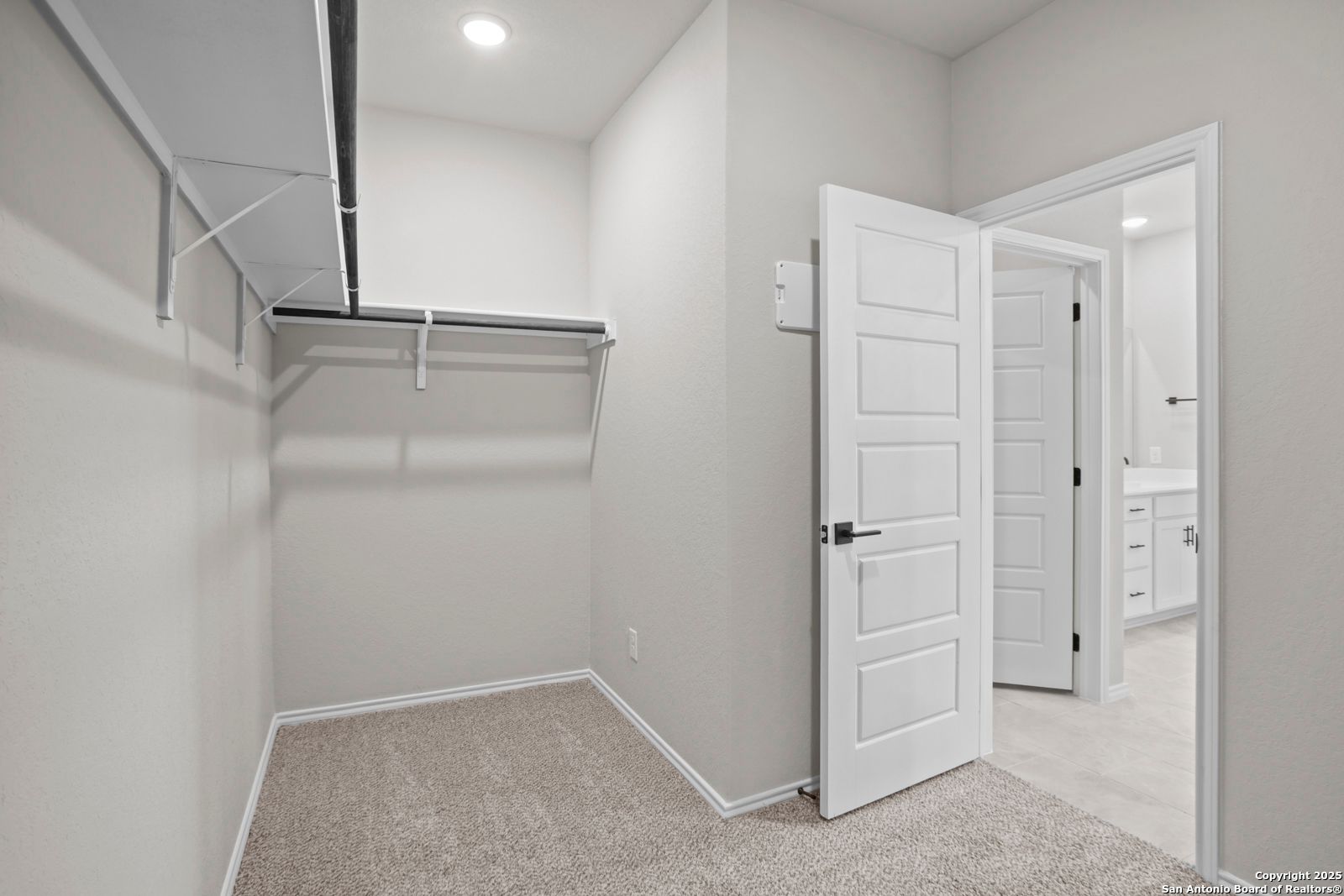 Spacious walk-in closet with built-in white shelving and open doors to master bath in Davidson Homes The Sequoia A, Converse, Texas