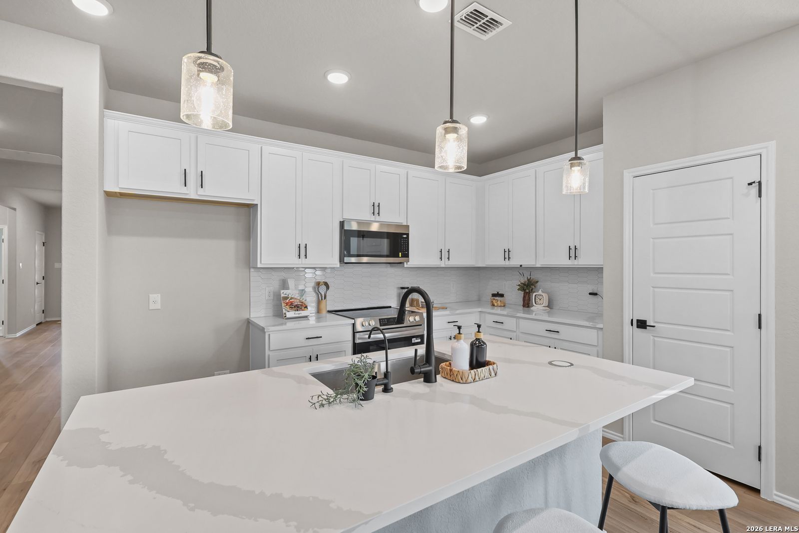 Modern kitchen with white cabinets, quartz island, and pendant lighting in The Daphne H floor plan, Hannah Heights, Seguin.