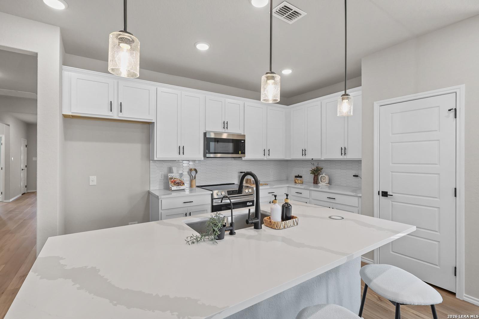 Modern kitchen with white cabinets, quartz island, and pendant lighting in The Daphne H floor plan, Hannah Heights, Seguin.