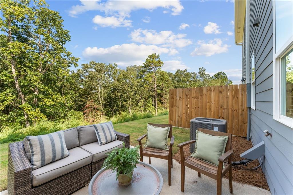 Cozy outdoor patio with wicker sofa, armchairs, potted fern, wooden privacy fence, lush green yard in Davidson Homes The Durant B, Emerson, Georgia