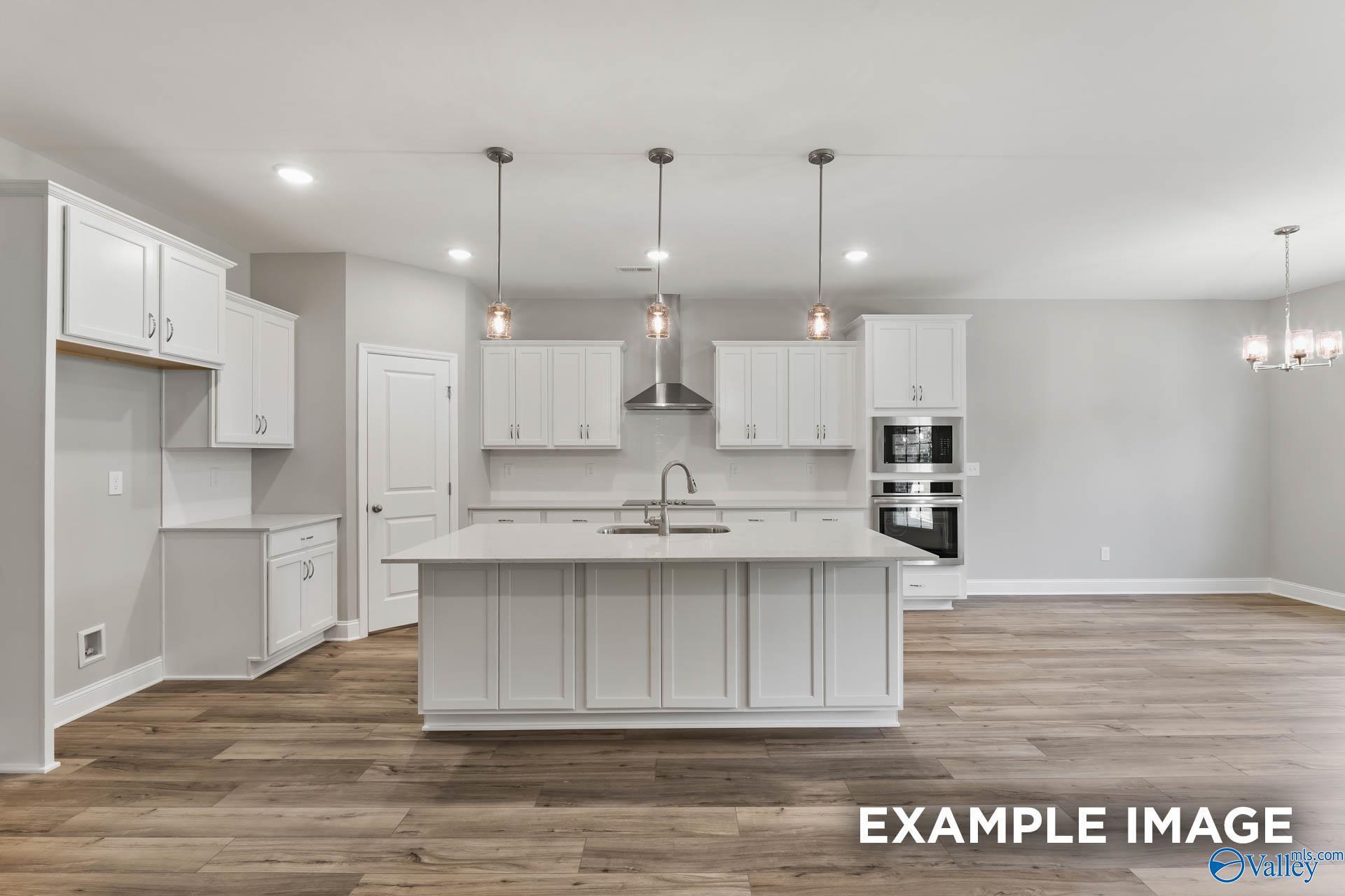 Modern white shaker kitchen with oversized island, double ovens, and hardwood floors in Davidson Homes The Rockford, Madison AL