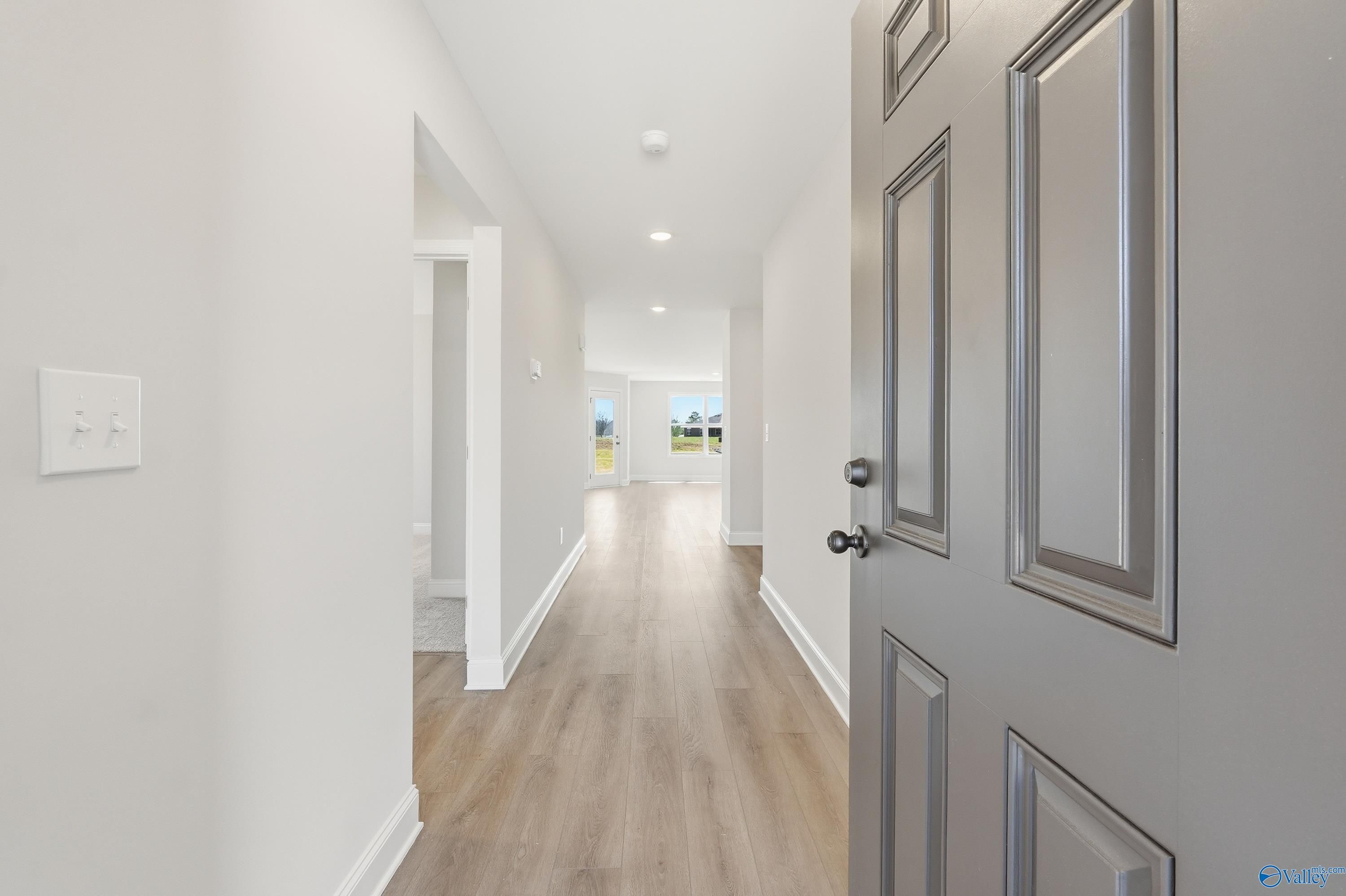 Bright entry hallway with light wood floors, white walls, and open bedroom door in Davidson Homes The Franklin V, Athens, Alabama