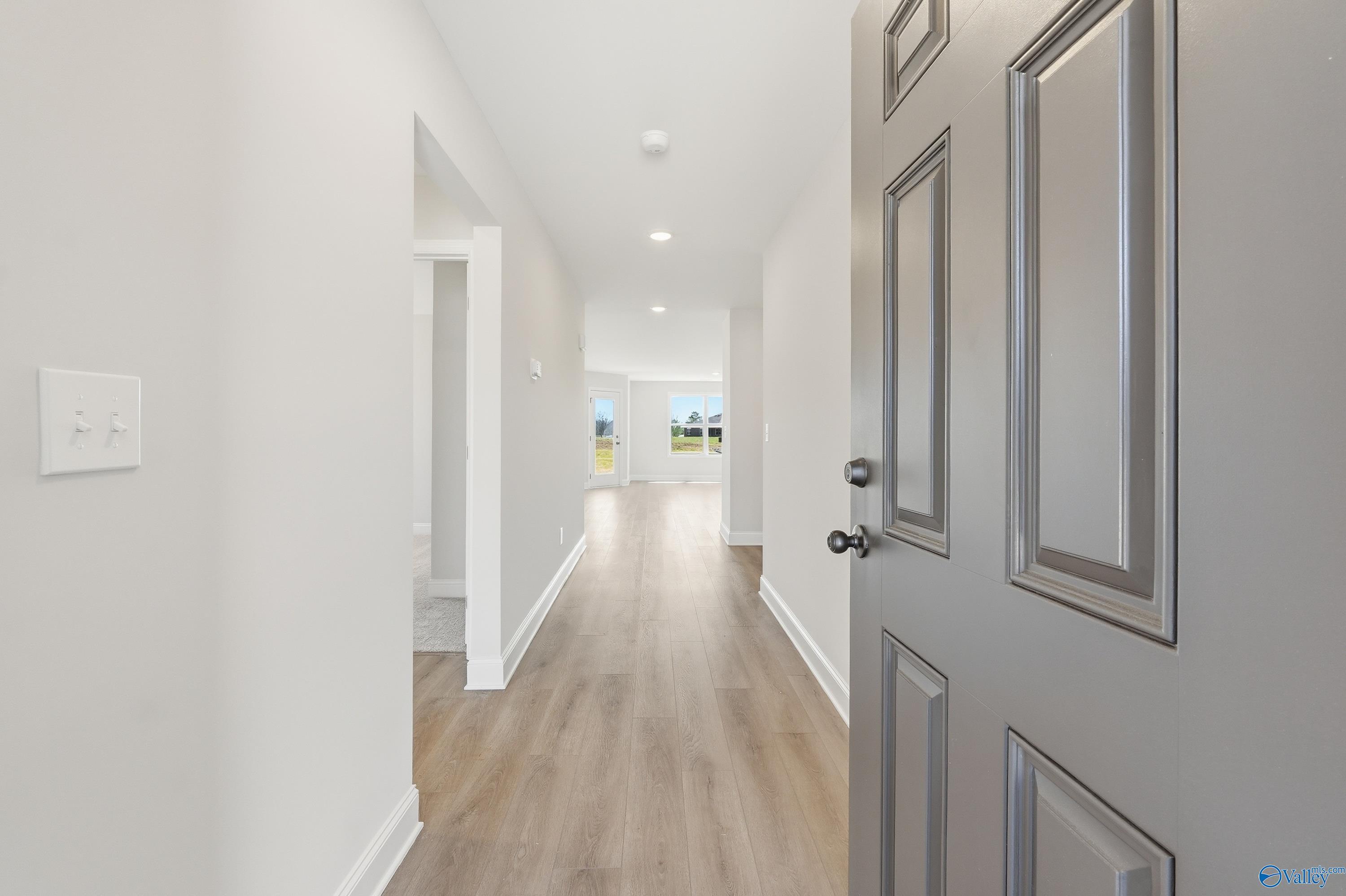 Bright entry hallway with light wood floors, white walls, and open bedroom door in Davidson Homes The Franklin V, Athens, Alabama