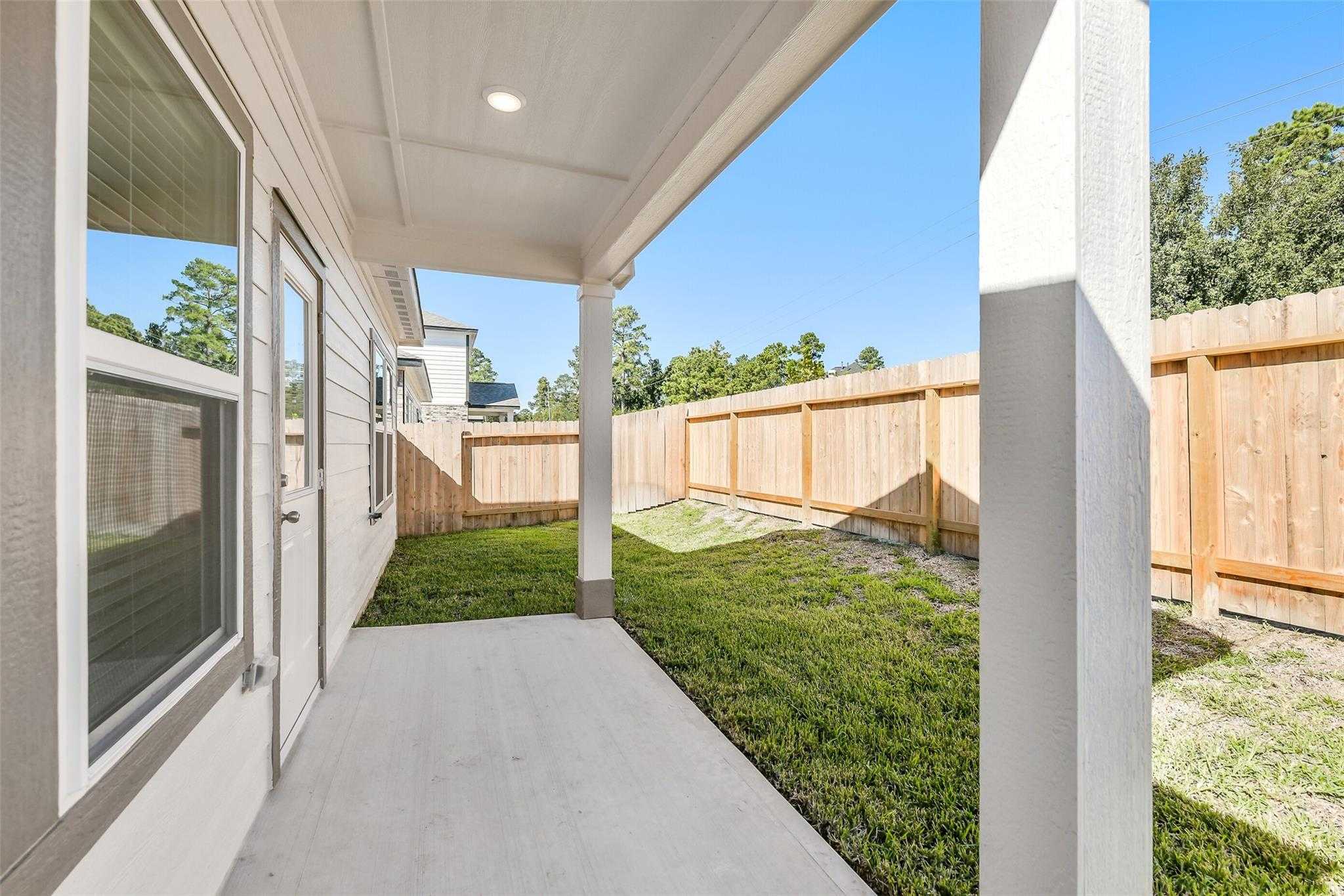 Covered side porch with wood privacy fence and green lawn in The Blanco E 4-bedroom home, Lakes at Black Oak, Magnolia, Texas