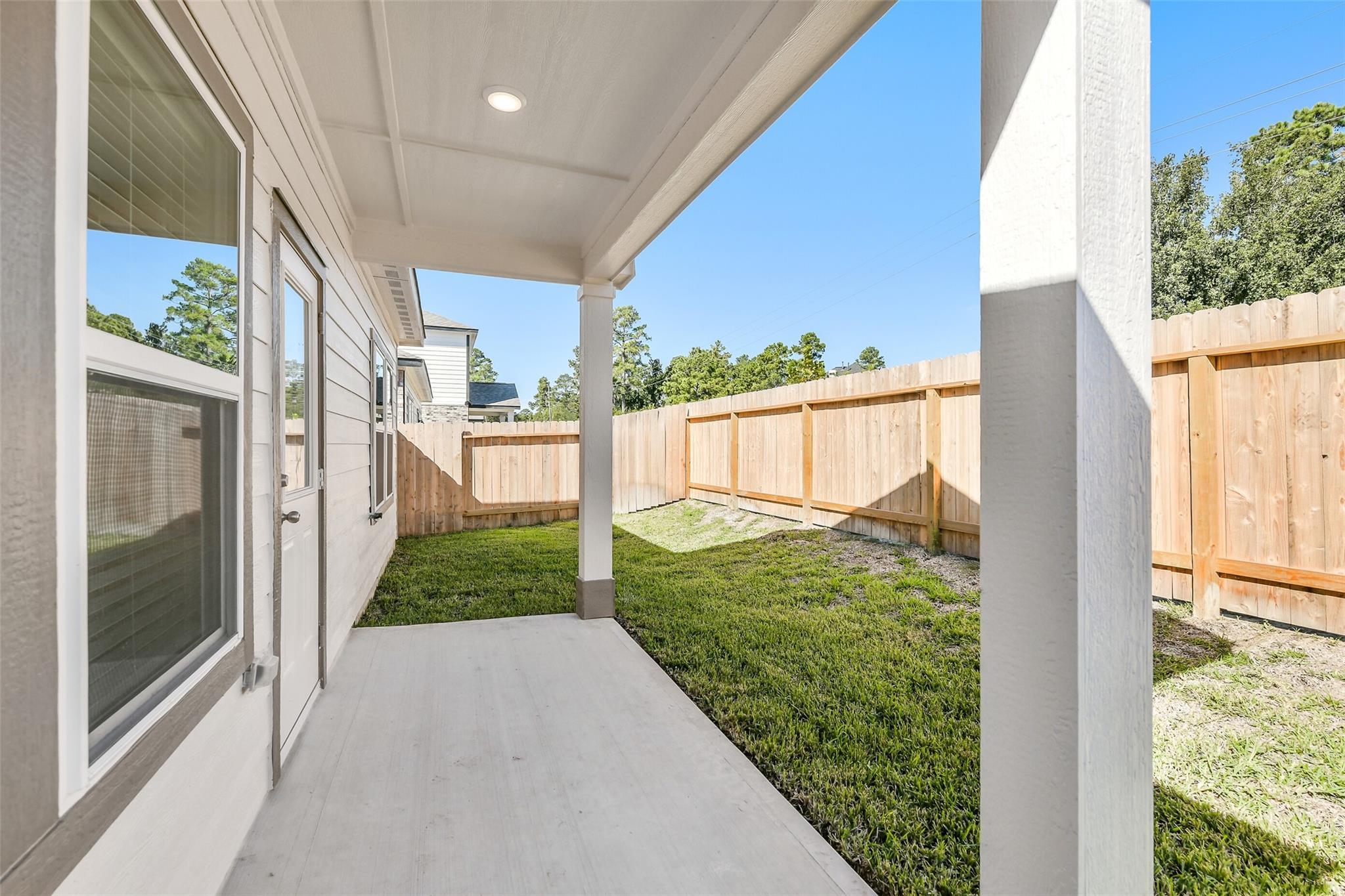 Covered side porch with wood privacy fence and green lawn in The Blanco E 4-bedroom home, Lakes at Black Oak, Magnolia, Texas