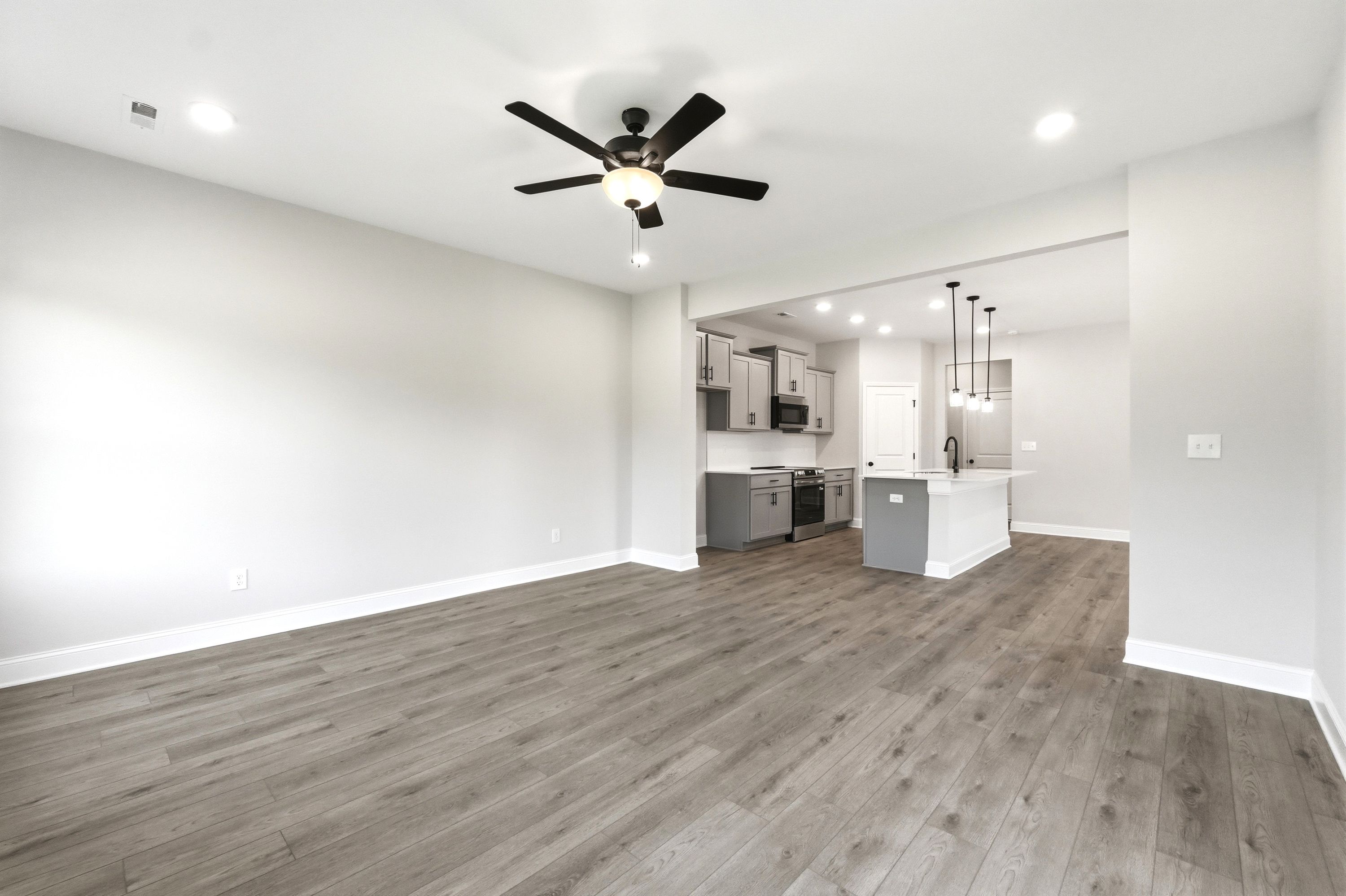 Open-concept living area and kitchen with modern grey cabinets and island in The Russell A floor plan by Davidson Homes.