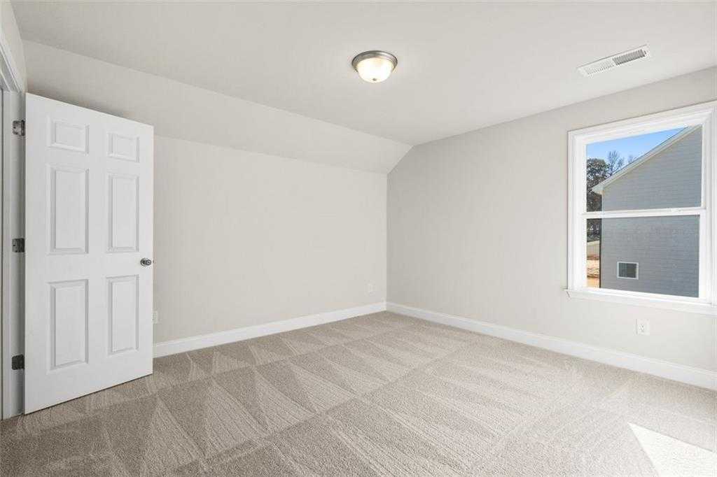 Bright secondary bedroom with sloped ceiling, light gray walls, white door, and patterned carpet in The Ash C at Wehunt Meadows, Hoschton