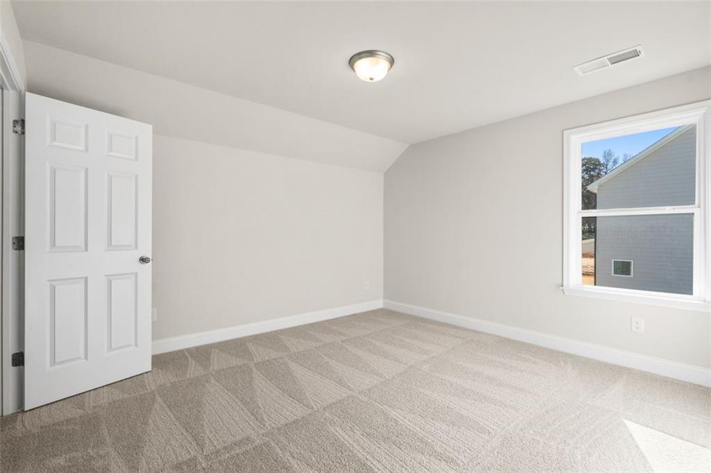 Bright secondary bedroom with sloped ceiling, light gray walls, white door, and patterned carpet in The Ash C at Wehunt Meadows, Hoschton