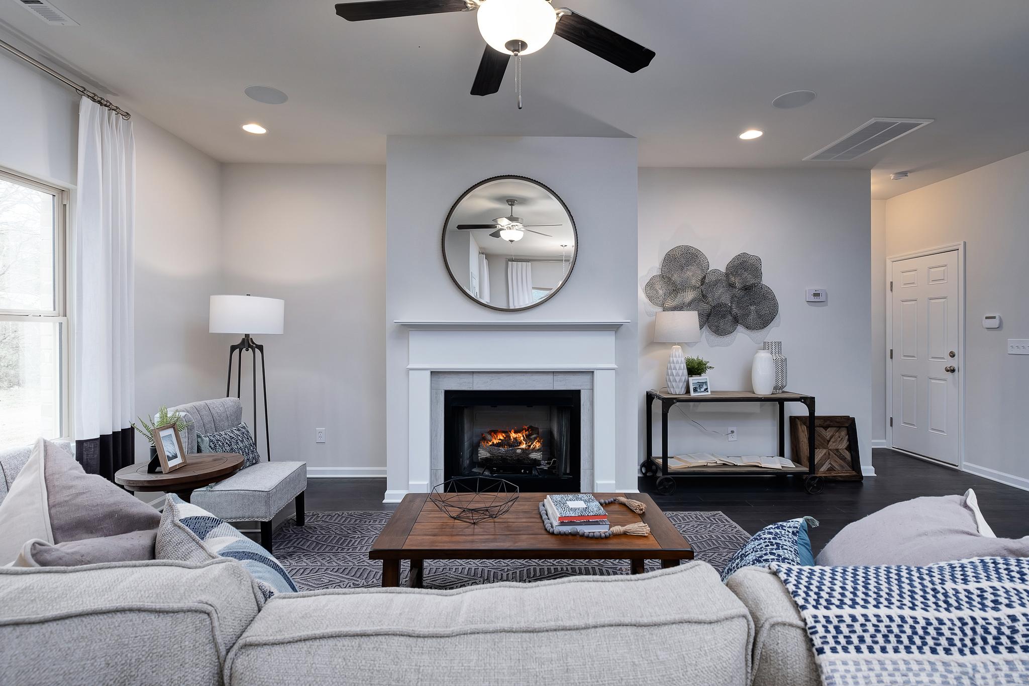 Modern living room with white fireplace, round mirror, gray sofa, coffee table, and ceiling fan at The Reserve at Overton in Hampton Cove AL
