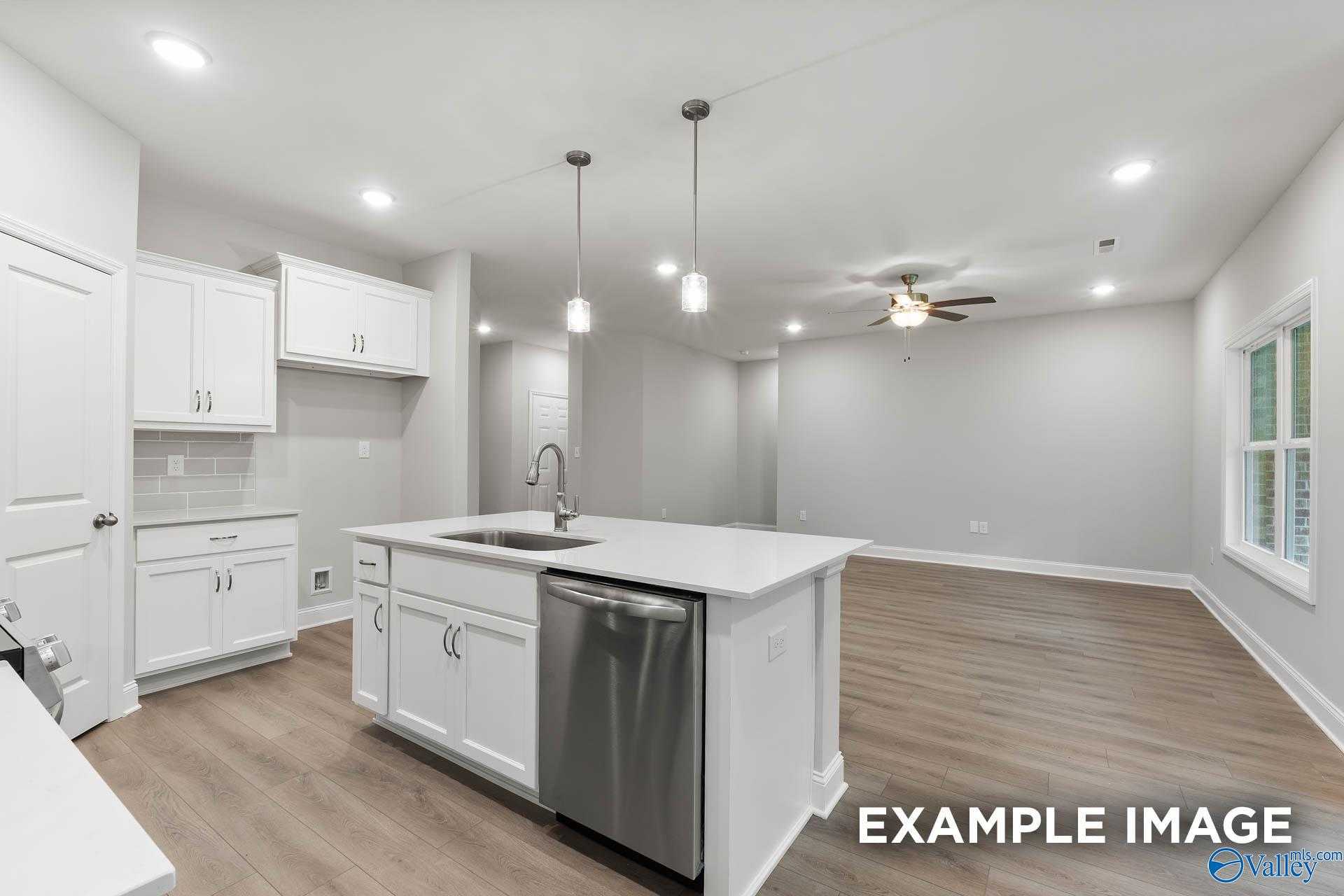 Modern open-concept kitchen with white shaker cabinets, large island sink, and stainless dishwasher in The Asheville C home, Huntsville AL