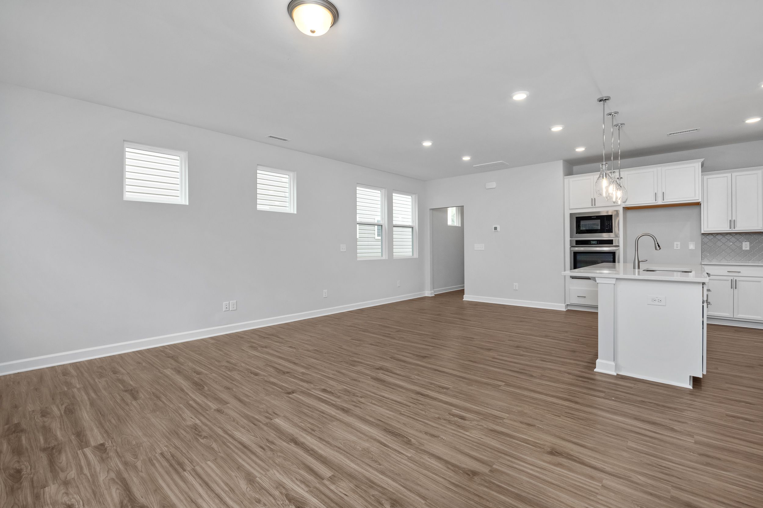 Open-concept living and kitchen area in The Durham featuring modern white cabinetry, wood-look flooring, and recessed lighting.