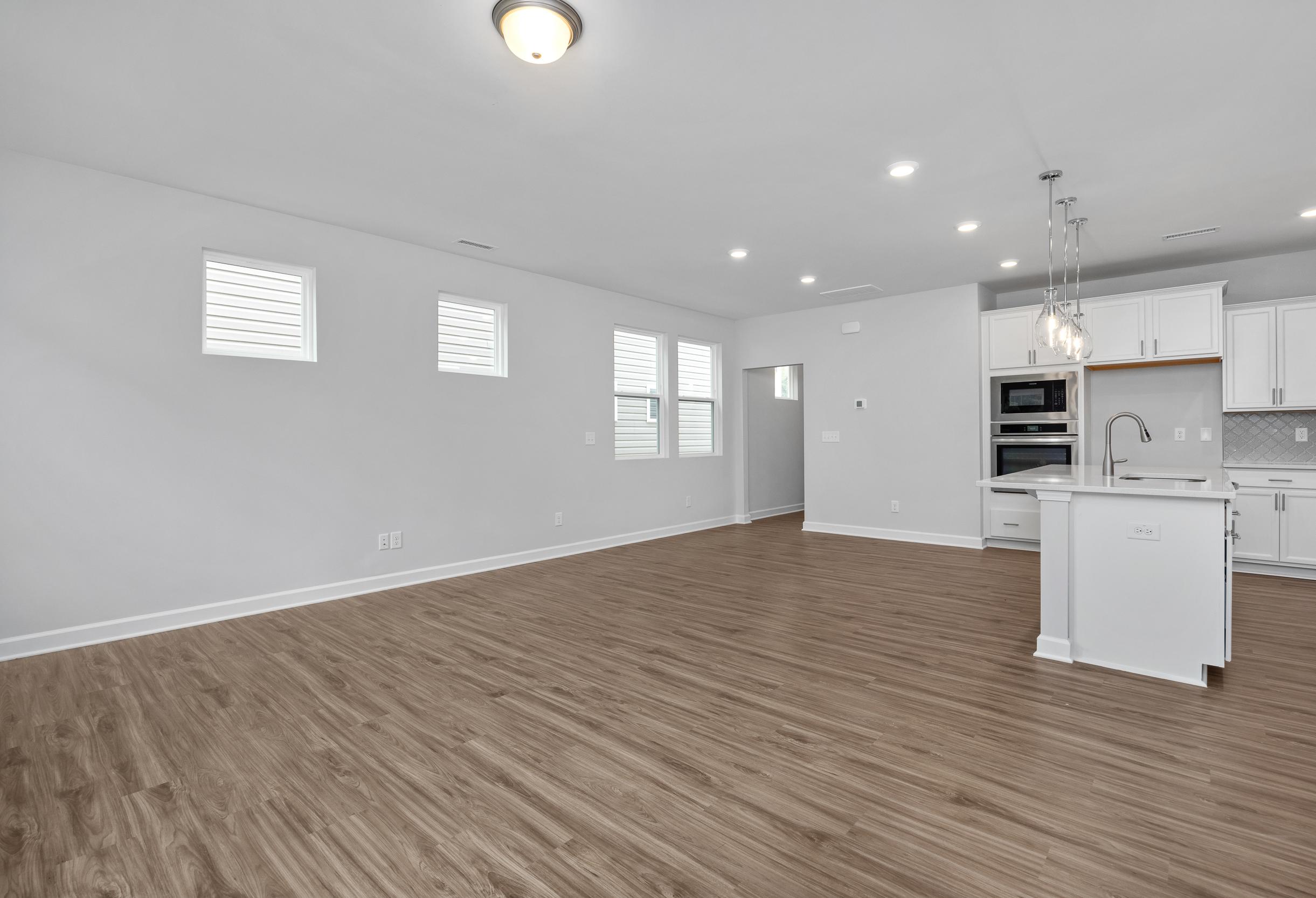 Open-concept living and kitchen area in The Durham featuring modern white cabinetry, wood-look flooring, and recessed lighting.