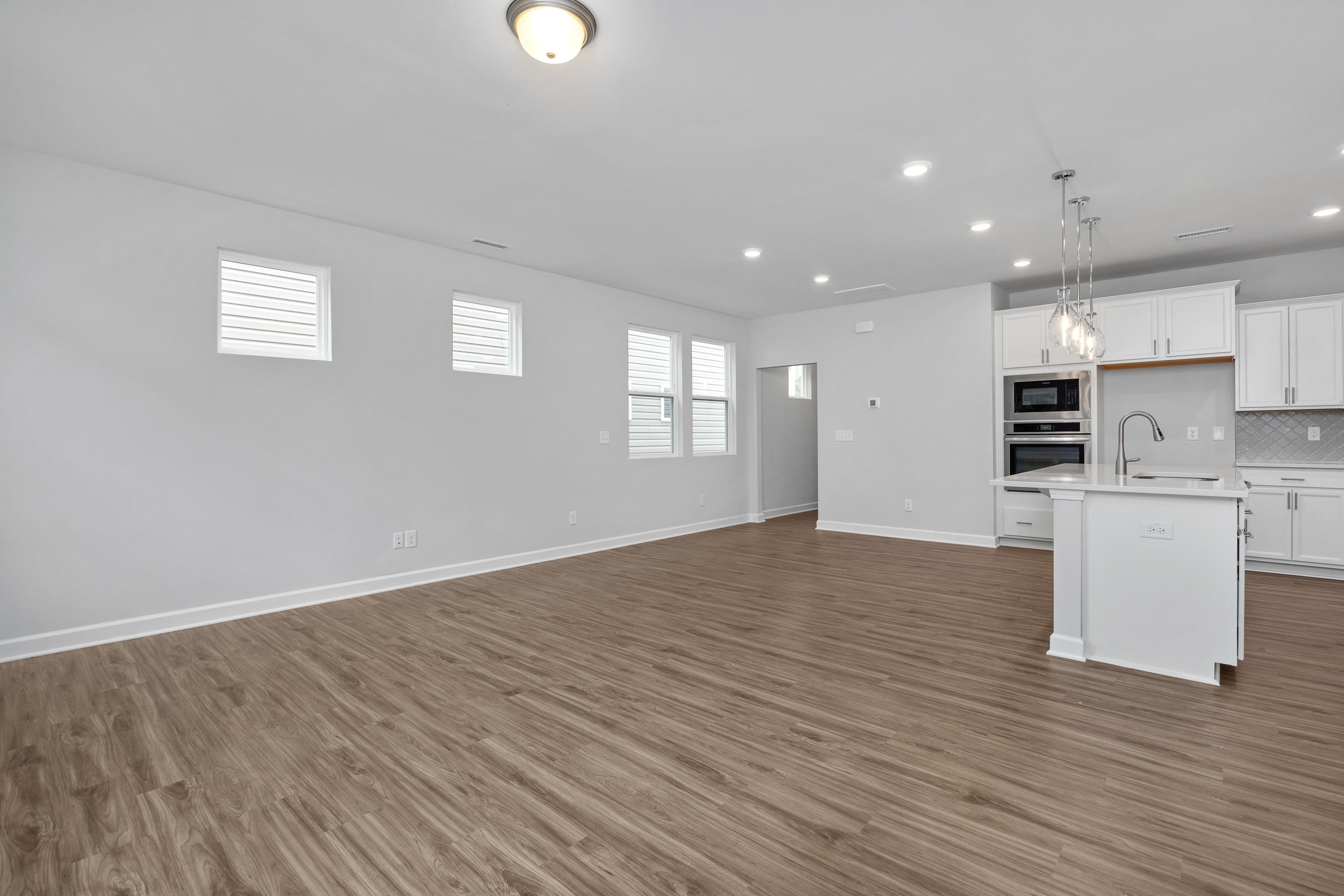 Open-concept living and kitchen area in The Durham featuring modern white cabinetry, wood-look flooring, and recessed lighting.