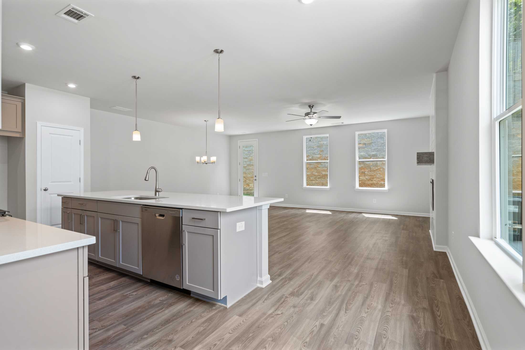 Spacious open-concept kitchen in The Cary A with white quartz island, gray cabinets, hardwood floors, and large windows