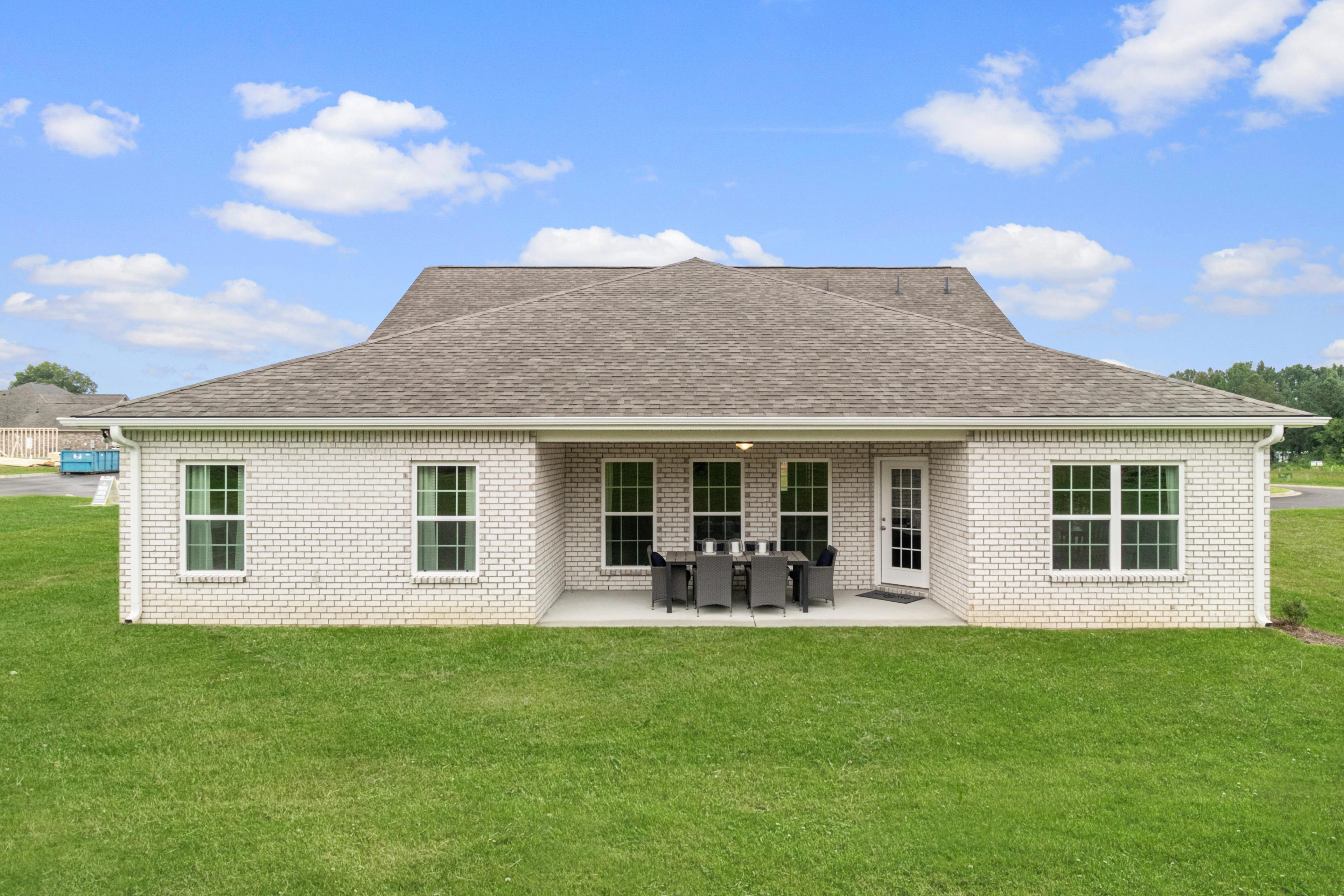 White brick home rear with covered patio, French doors, outdoor dining set, and lush green lawn at North Ridge in Cullman Alabama