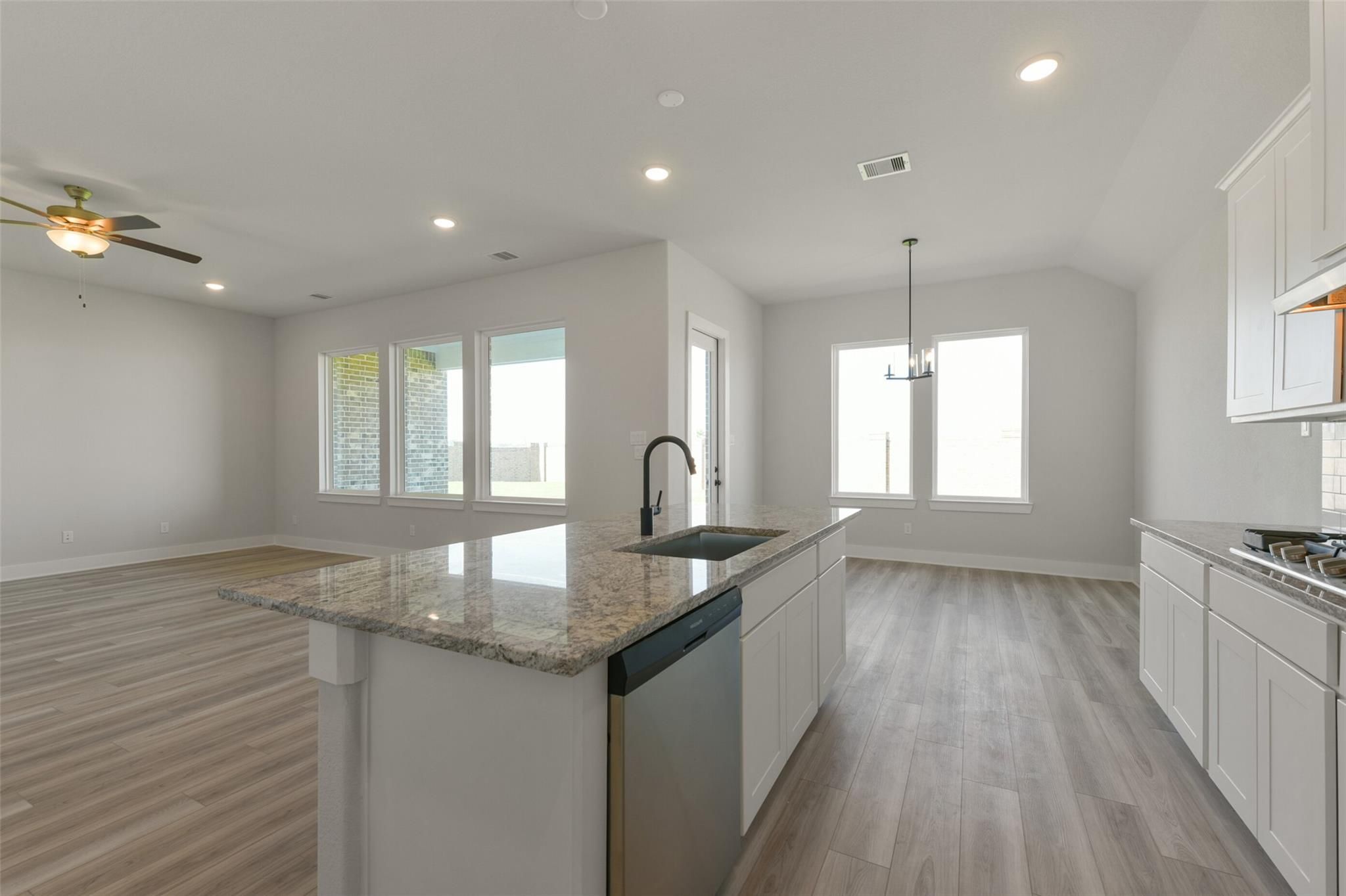 Modern open-concept kitchen with white cabinets, granite island sink, stainless dishwasher in Davidson Homes The Edward C, Lago Mar, Texas City