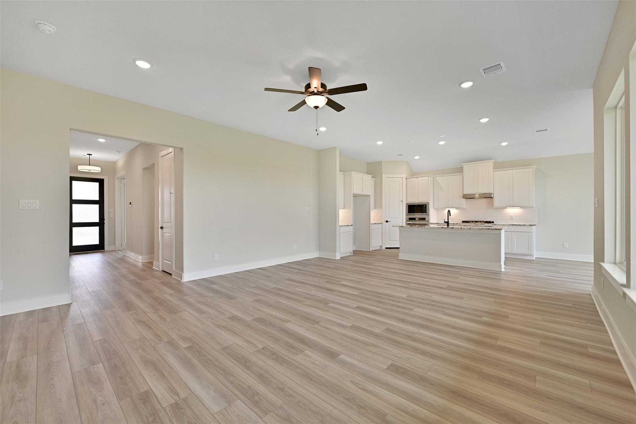 Open-concept living and kitchen with white cabinets, island sink, and ceiling fan in Davidson Homes The Edward C, Texas City