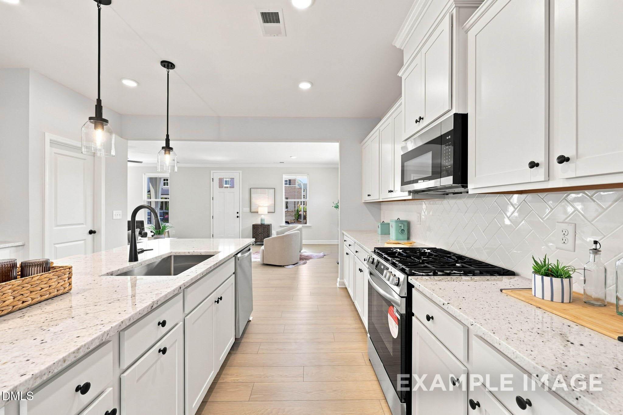 Bright white kitchen with granite countertops, gas range, island sink, and pendant lights in Davidson Homes The Harris A, Knightdale, NC