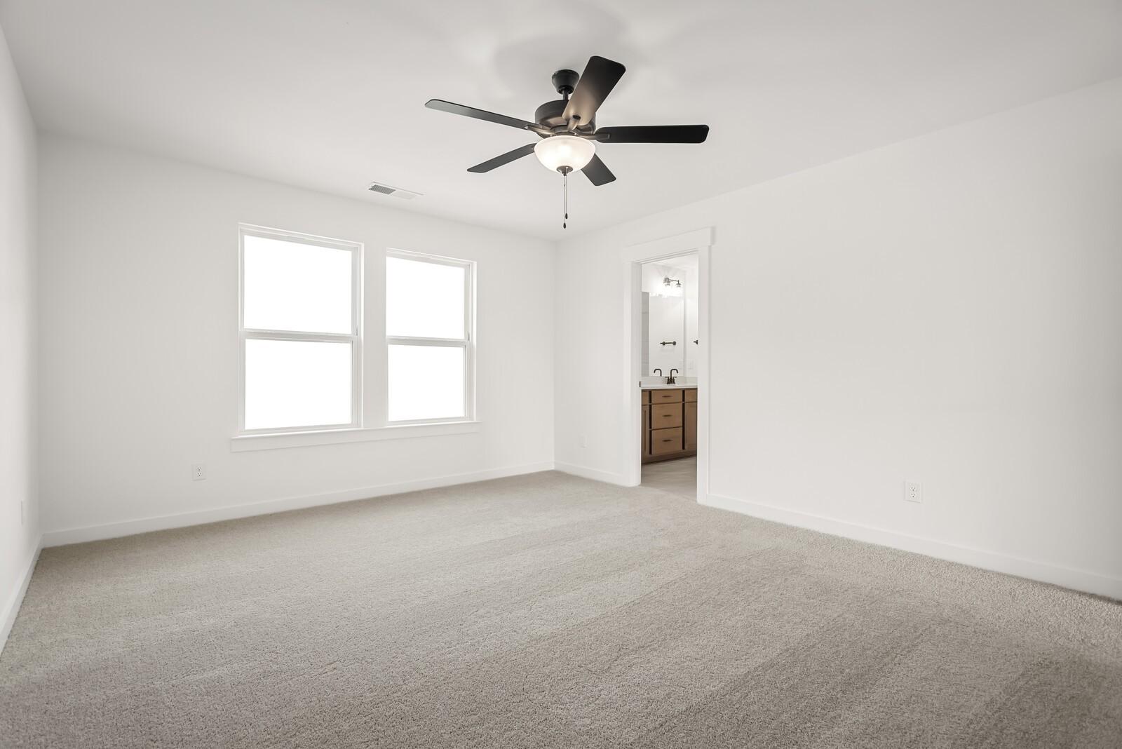 Spacious bedroom with ceiling fan, large windows, and adjacent bath in Davidson Homes The Logan C, Gallatin, TN