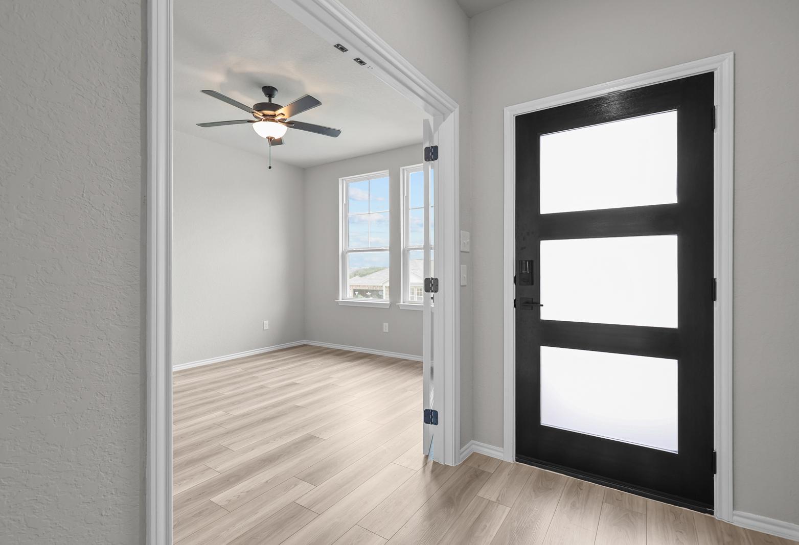 Modern entryway of The Glenwood D featuring a contemporary black door and bright, open-concept flex room with wood flooring.
