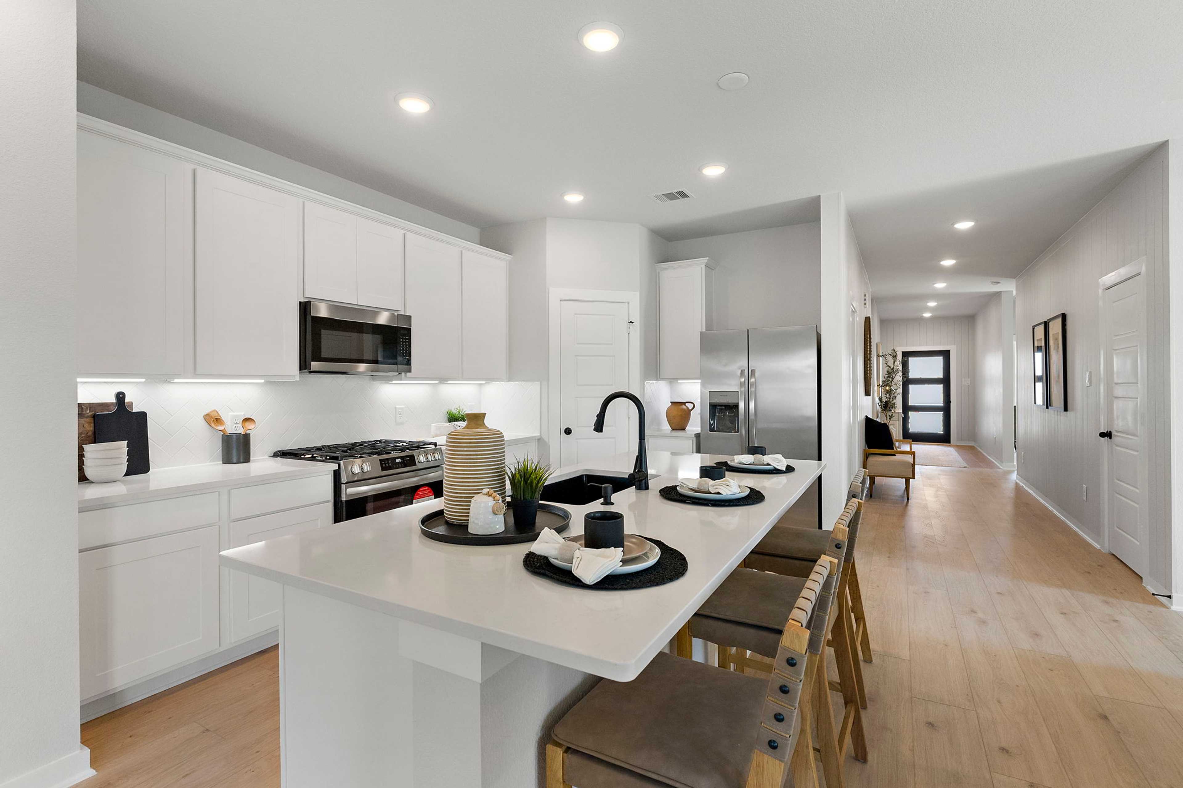 Modern white kitchen at Sundance Cove in Crosby TX with large island, stainless appliances and hardwood floors