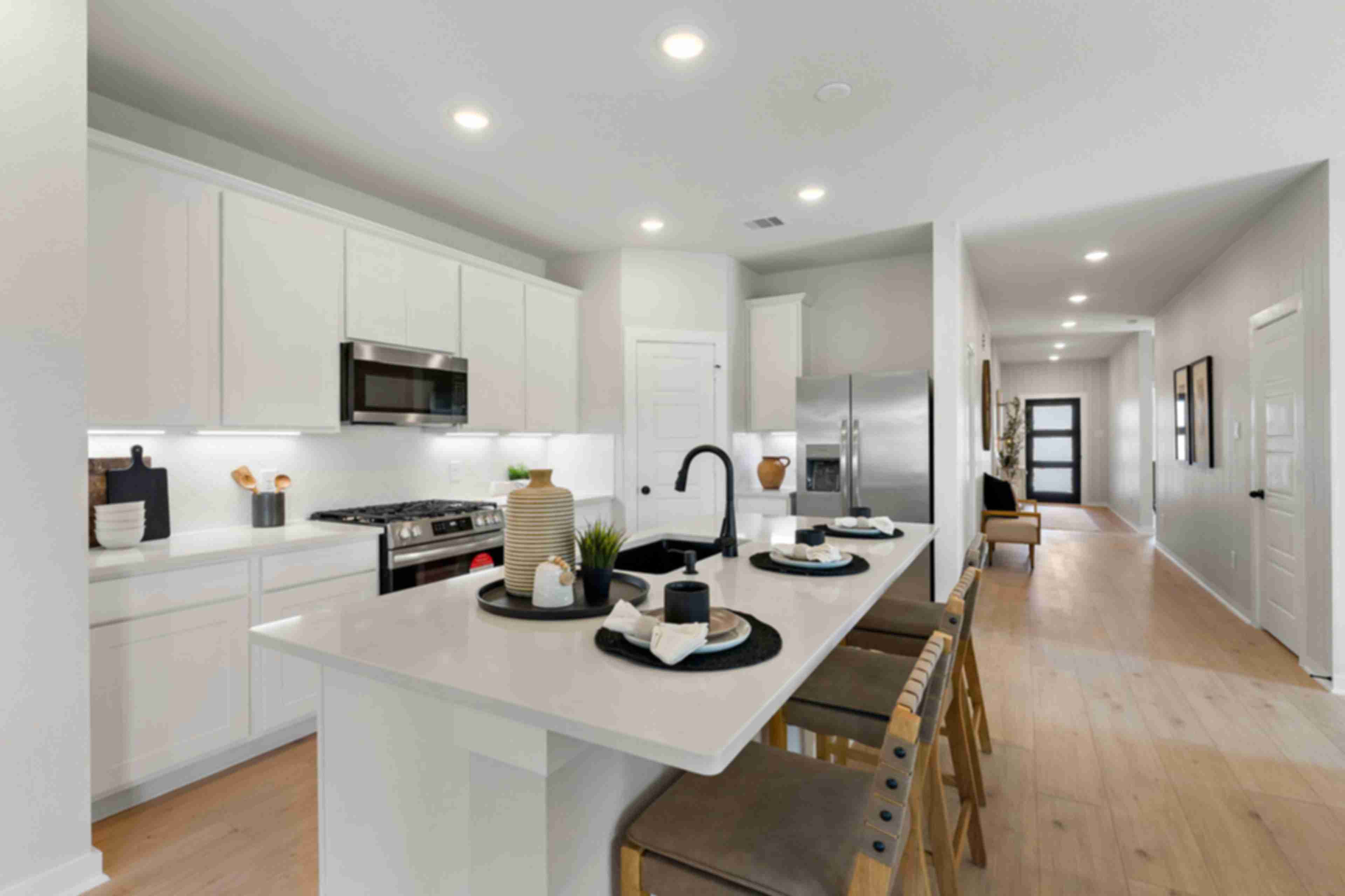 Modern white kitchen with island, stainless steel appliances, and wood floors at Sundance Cove in Crosby, Texas