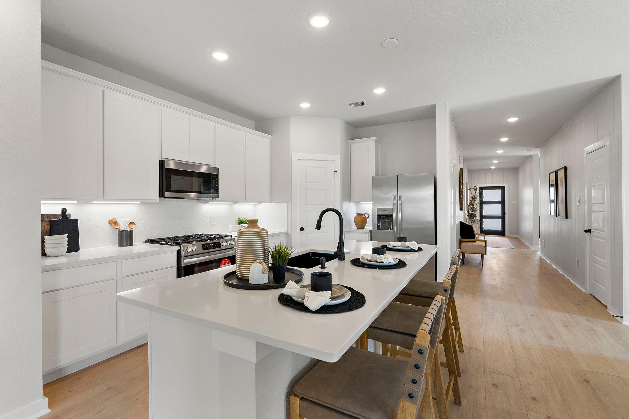 Modern white kitchen with island, stainless appliances, and hardwood floors at Sundance Cove in Crosby, Texas by Davidson Homes