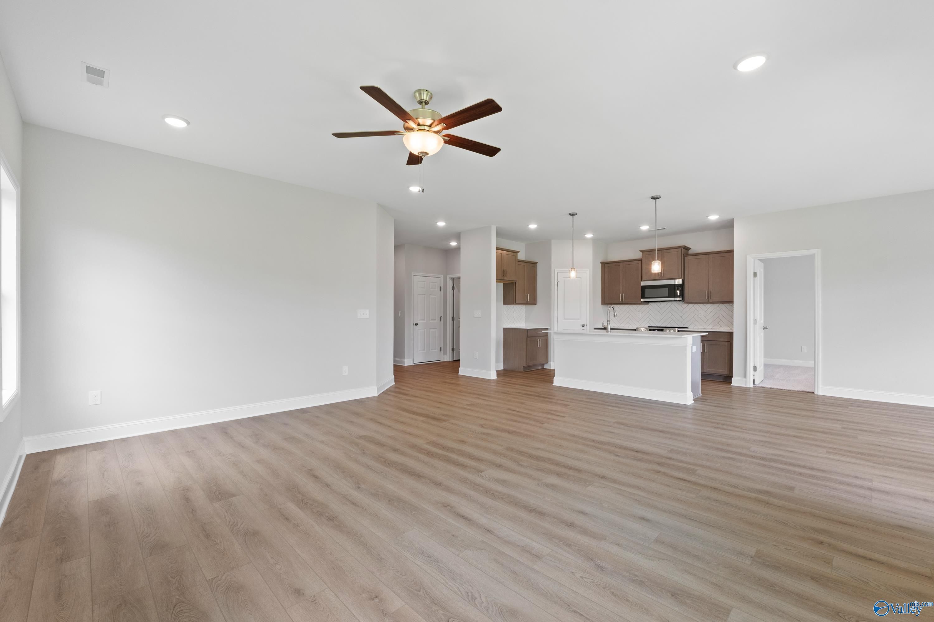 Open-concept kitchen and living area with ceiling fan, hardwood floors, white cabinets, and island in Davidson Homes The Franklin C, Harvest, Alabama