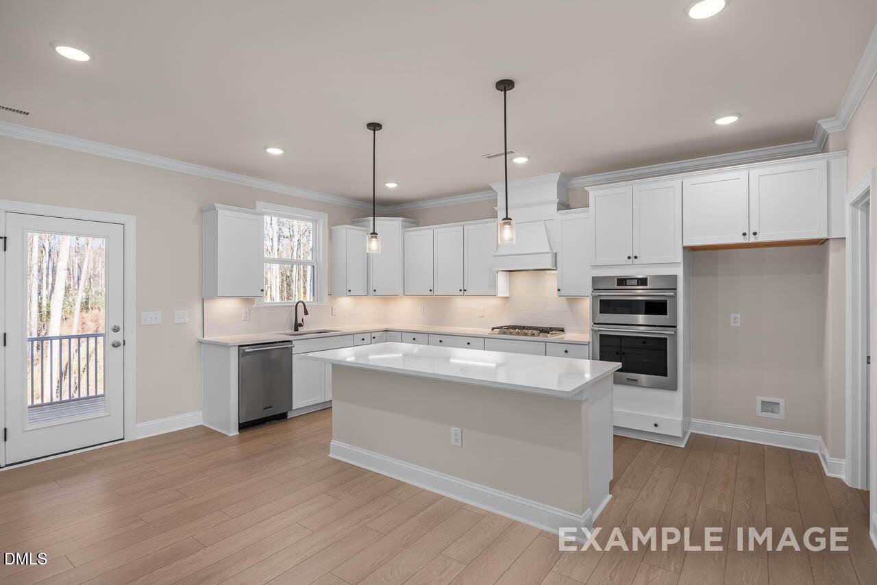 Bright modern kitchen with white cabinets, large island, stainless appliances, and deck access in The Crawford D, Angier, NC