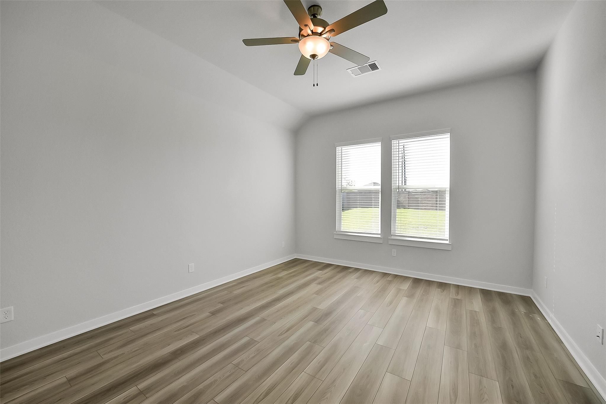 Bright secondary bedroom featuring wood laminate flooring, ceiling fan, and dual windows with yard view in Davidson Homes The Acadia A, Katy TX