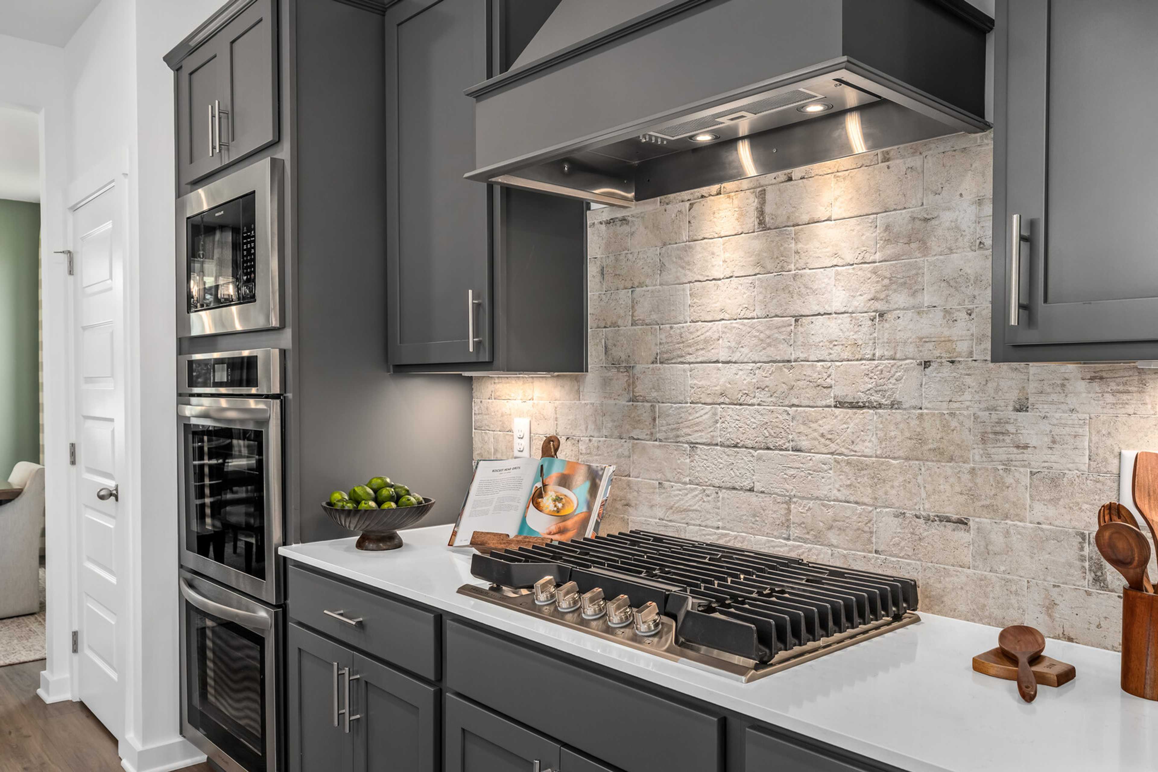 Modern kitchen in Calista Farms White House TN with dark gray cabinets, white quartz counters, stainless steel gas range and subway tile backsplash