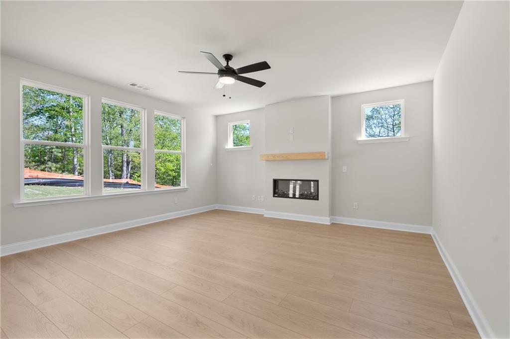 Bright living room with gas fireplace, wooden mantel, ceiling fan, and large windows overlooking trees in Davidson Homes The Hickory E, Buford, Georgia